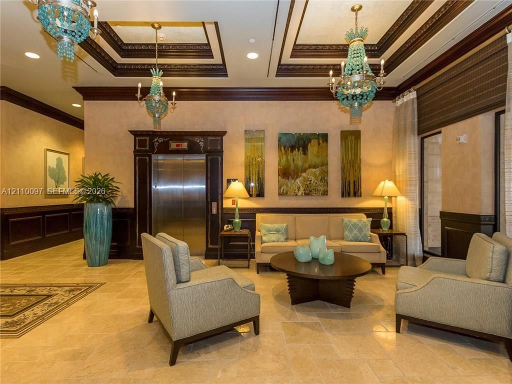 Tray ceilings with crown molding, stone tile flooring, stainless steel elevator, recessed lighting, and dual beaded-accent chandeliers