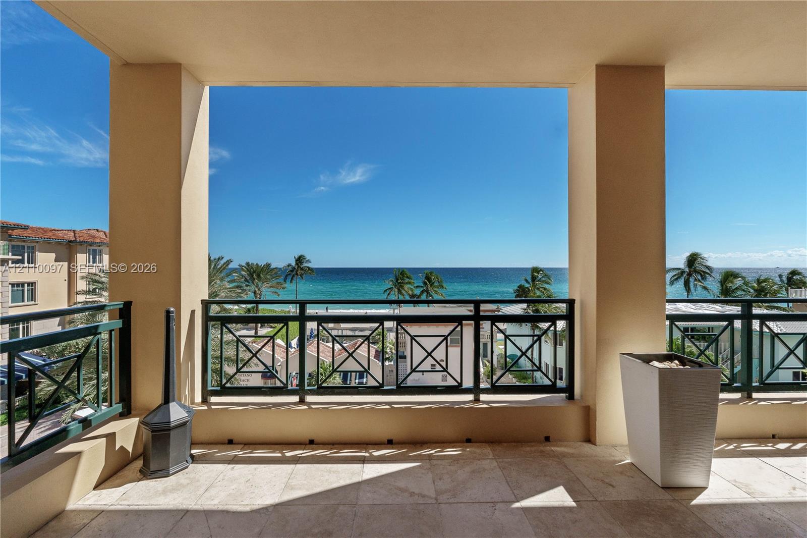 Covered balcony featuring stone flooring, a dark metal railing, and ocean scenery