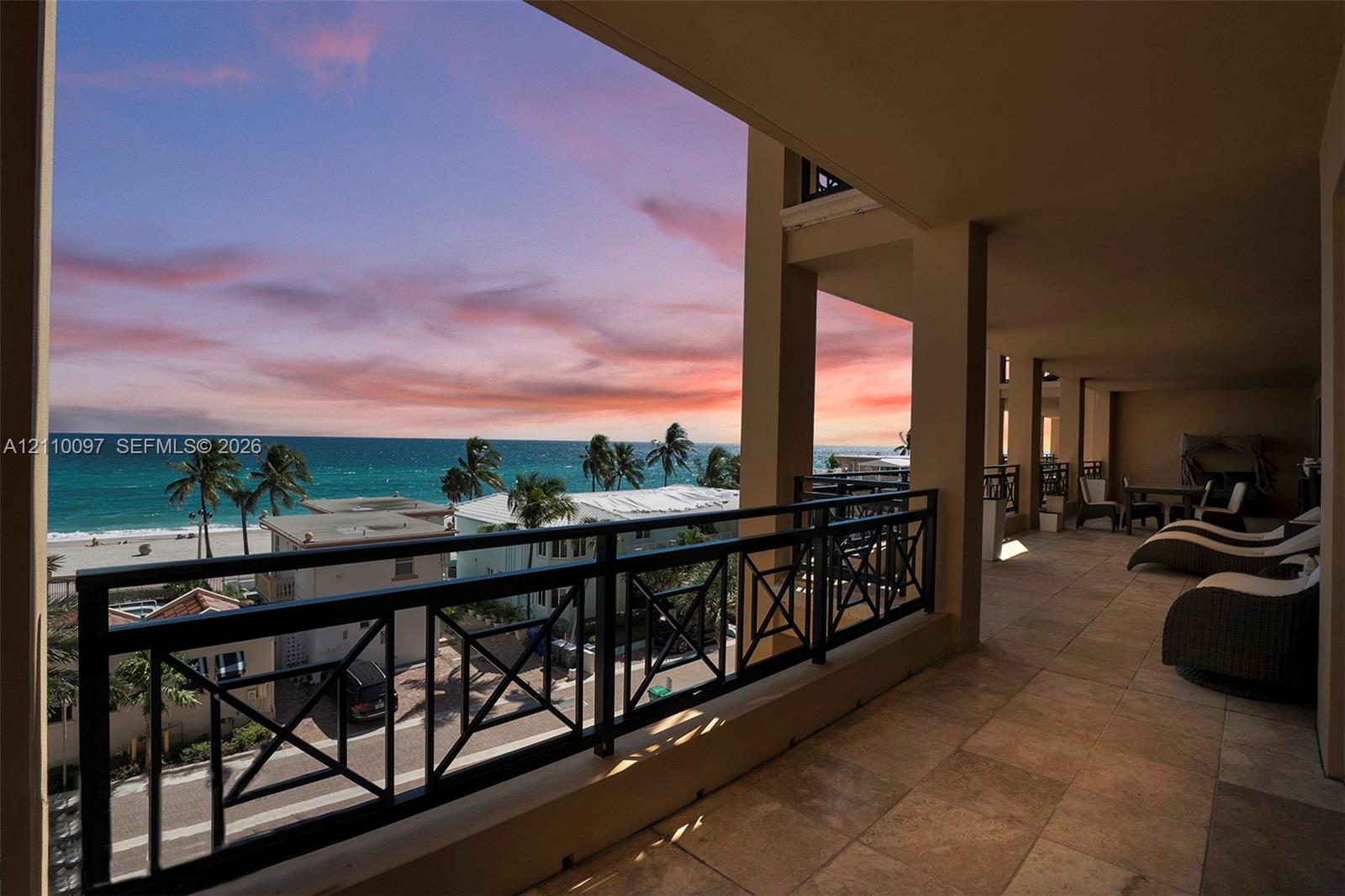 Covered balcony featuring natural stone tile flooring, a geometric metal railing, and expansive ocean and coastal scenery