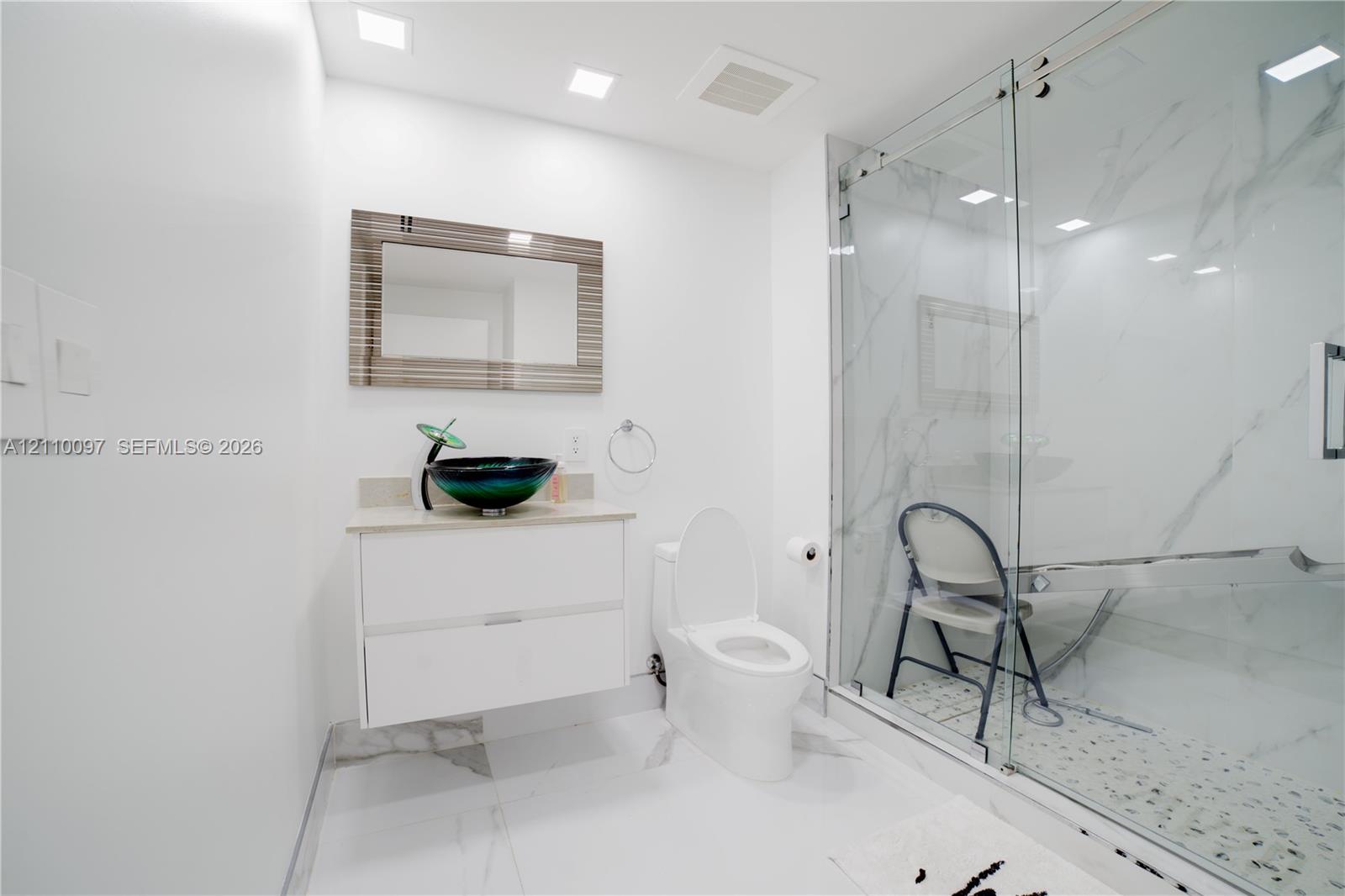 Bathroom featuring a floating vanity with a vessel sink, walk-in shower with stone-pattern wall tile, recessed lighting, and large-format flooring
