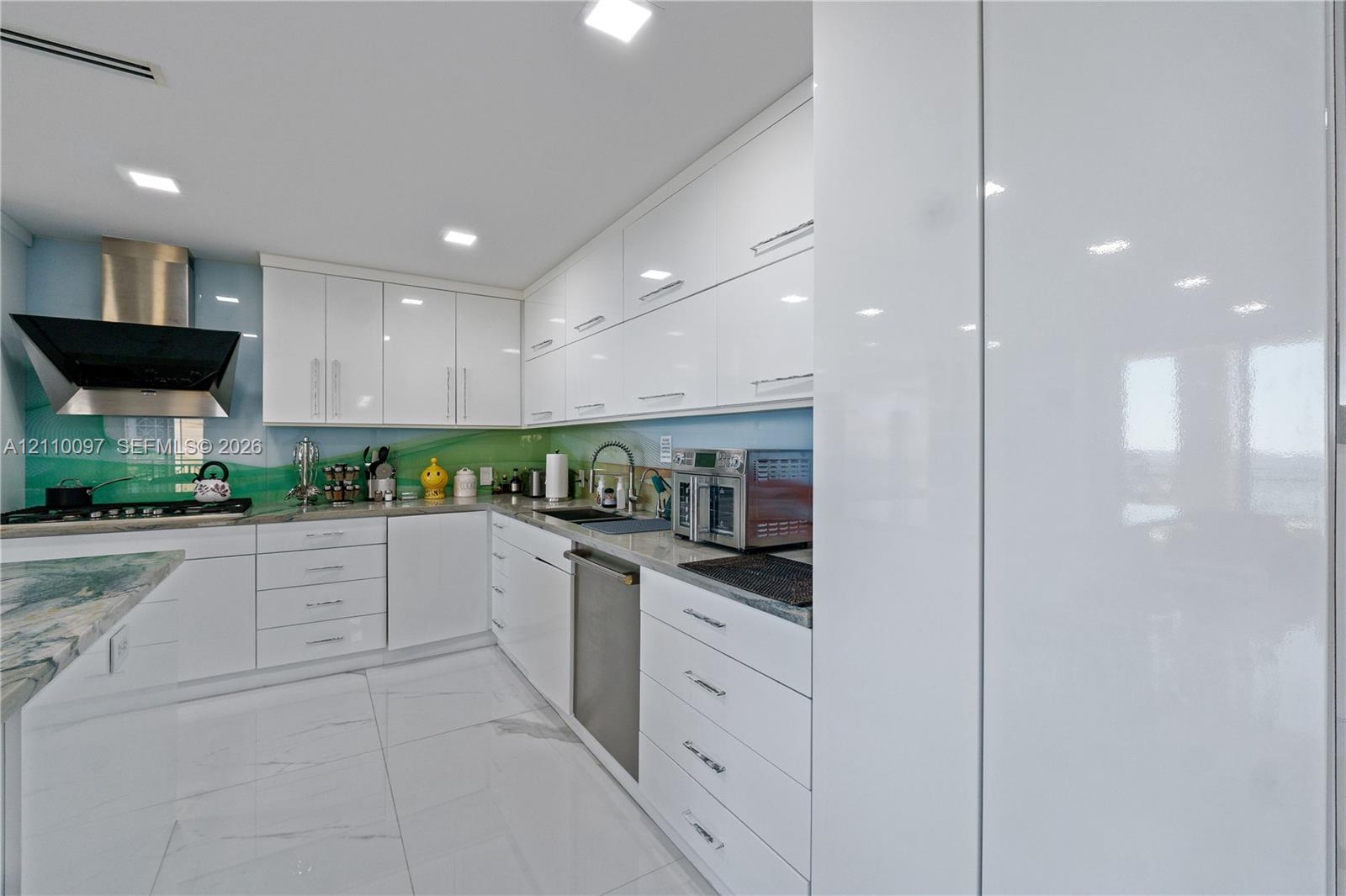 Modern kitchen featuring high-gloss cabinetry, stone countertops, integrated stainless steel appliances, a stainless steel range hood, and large-format tile flooring