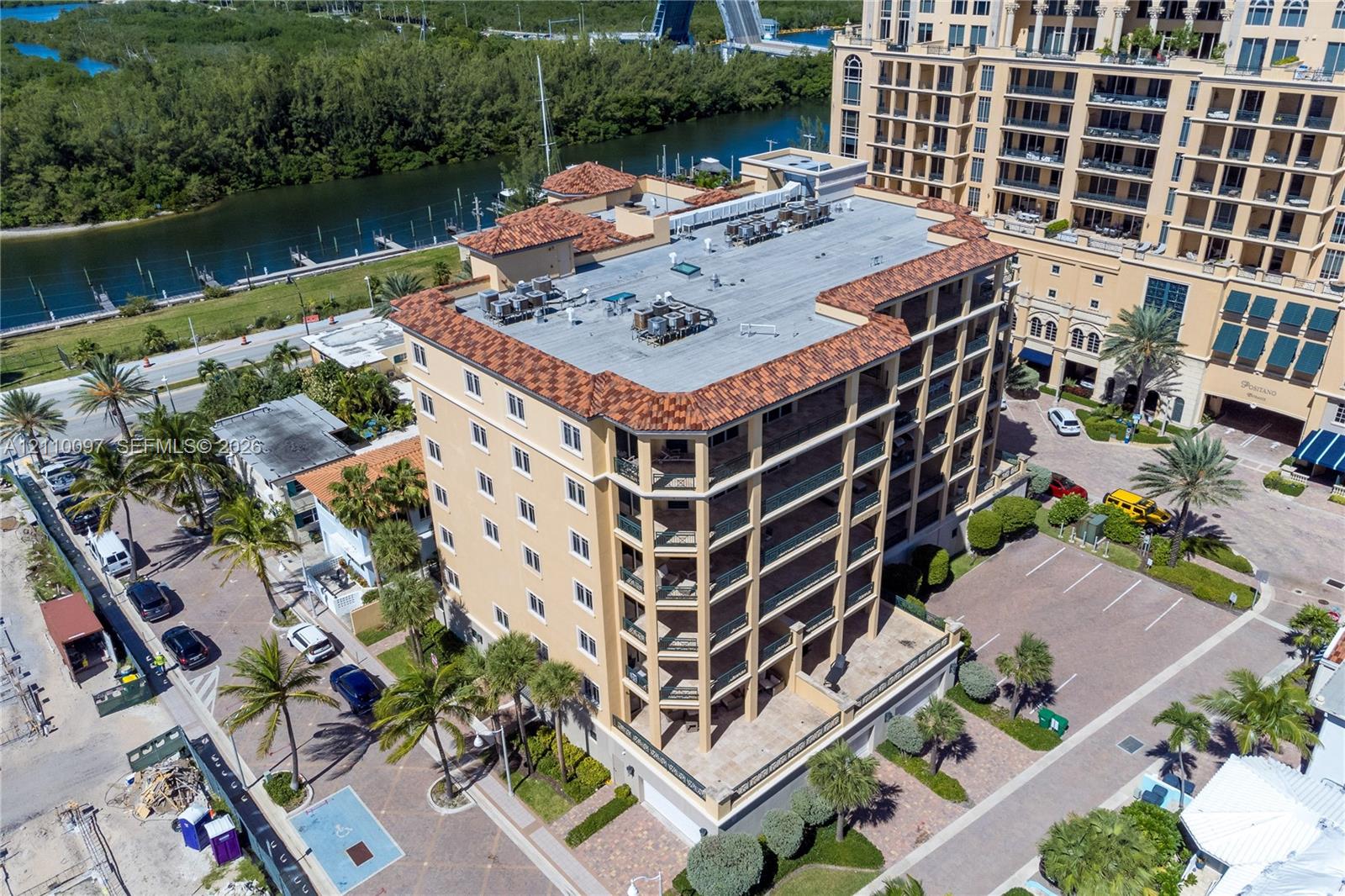 Mid-rise multi-story building featuring tile roofing, covered balconies, beige exterior facade, and paved surface parking Mid-rise multi-story building featuring tile roofing, covered balconies, beige exterior facade, and paved surface parking
