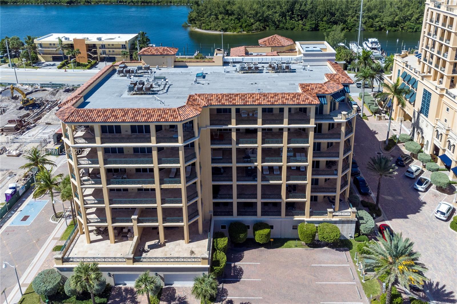 Multi-story building with a terracotta tile roof, structural balconies, paved surface parking, and exterior palm landscaping Multi-story building with a terracotta tile roof, structural balconies, paved surface parking, and exterior palm landscaping
