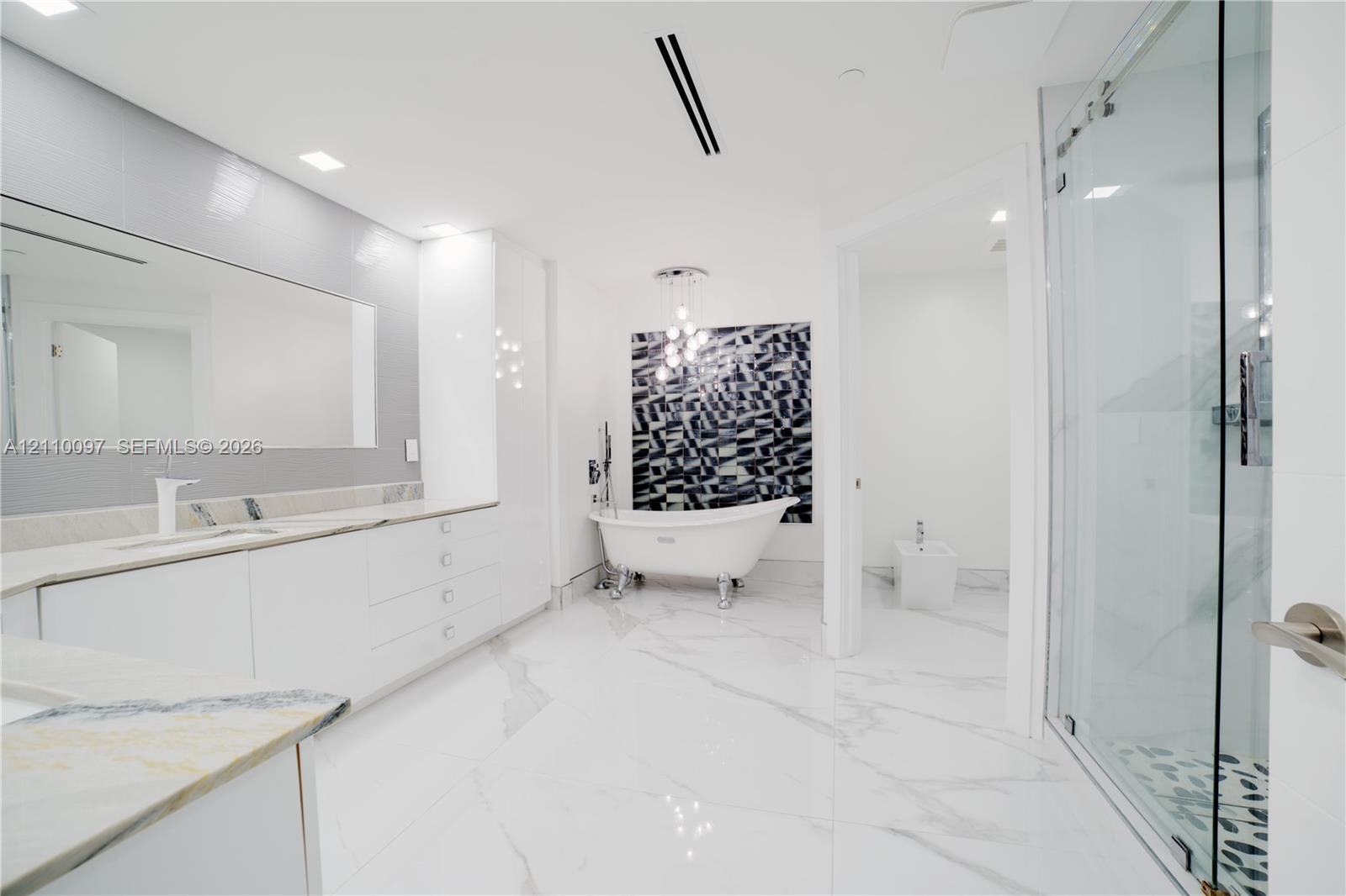 Bathroom featuring a claw-foot soaking tub, large format tile flooring with veining, glass-enclosed shower, expansive vanity with integrated sink, and modern pendant lighting
