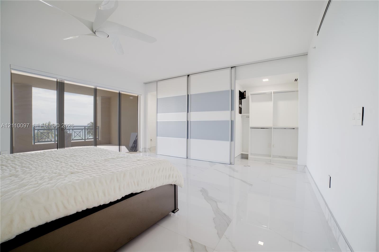 Large-format stone-finish flooring, floor-to-ceiling sliding glass doors, built-in dual-panel sliding wardrobe doors, ceiling-mounted multi-blade fan, and recessed lighting
