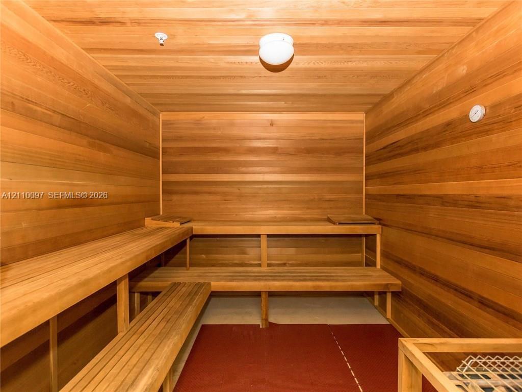 Sauna featuring full wood-paneled walls and ceiling, multi-level built-in wooden benches, and wall-mounted temperature gauge