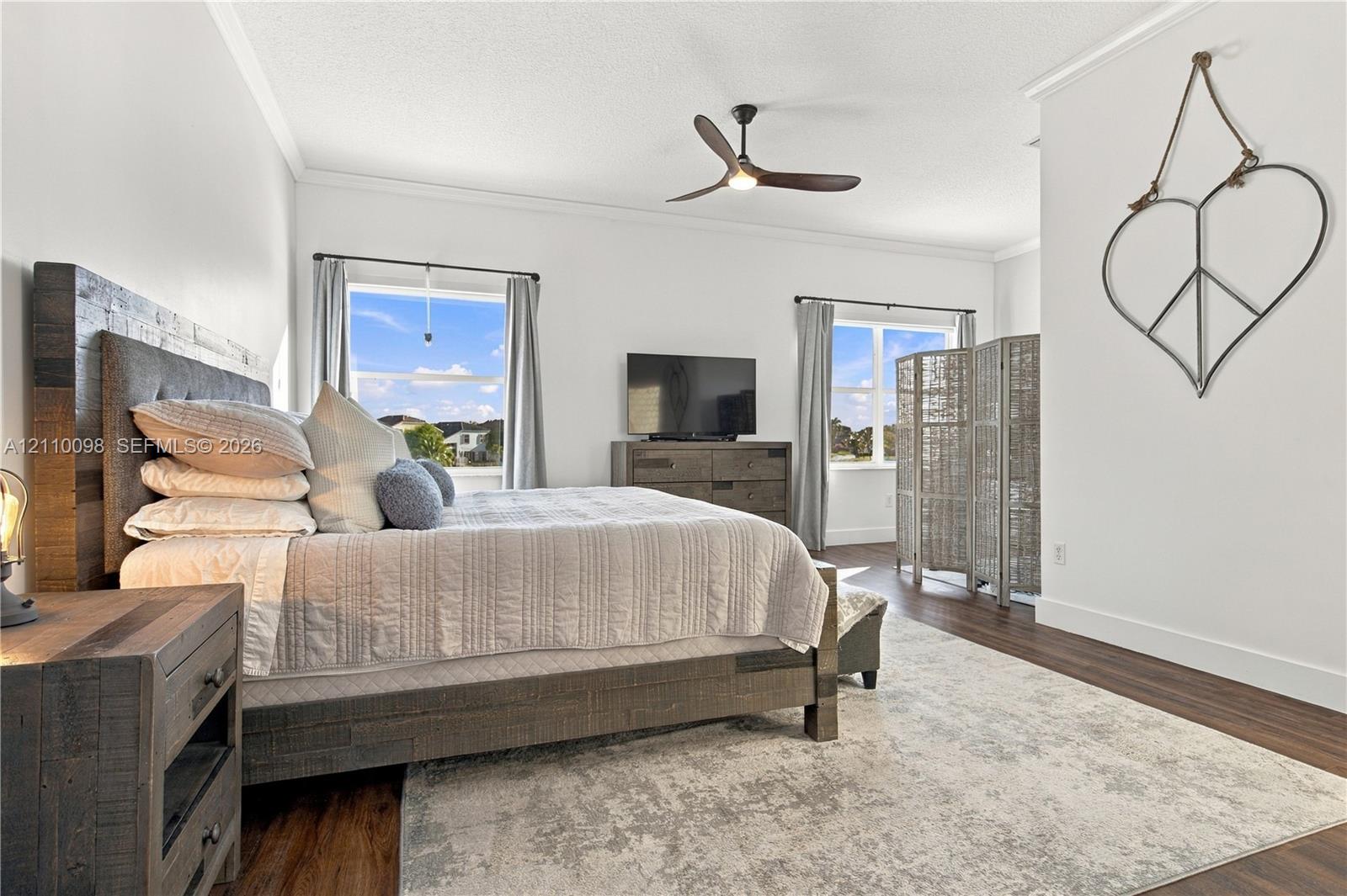 Spacious room featuring wood-finish flooring, crown molding, a multi-blade ceiling fan, and large windows with natural lighting
