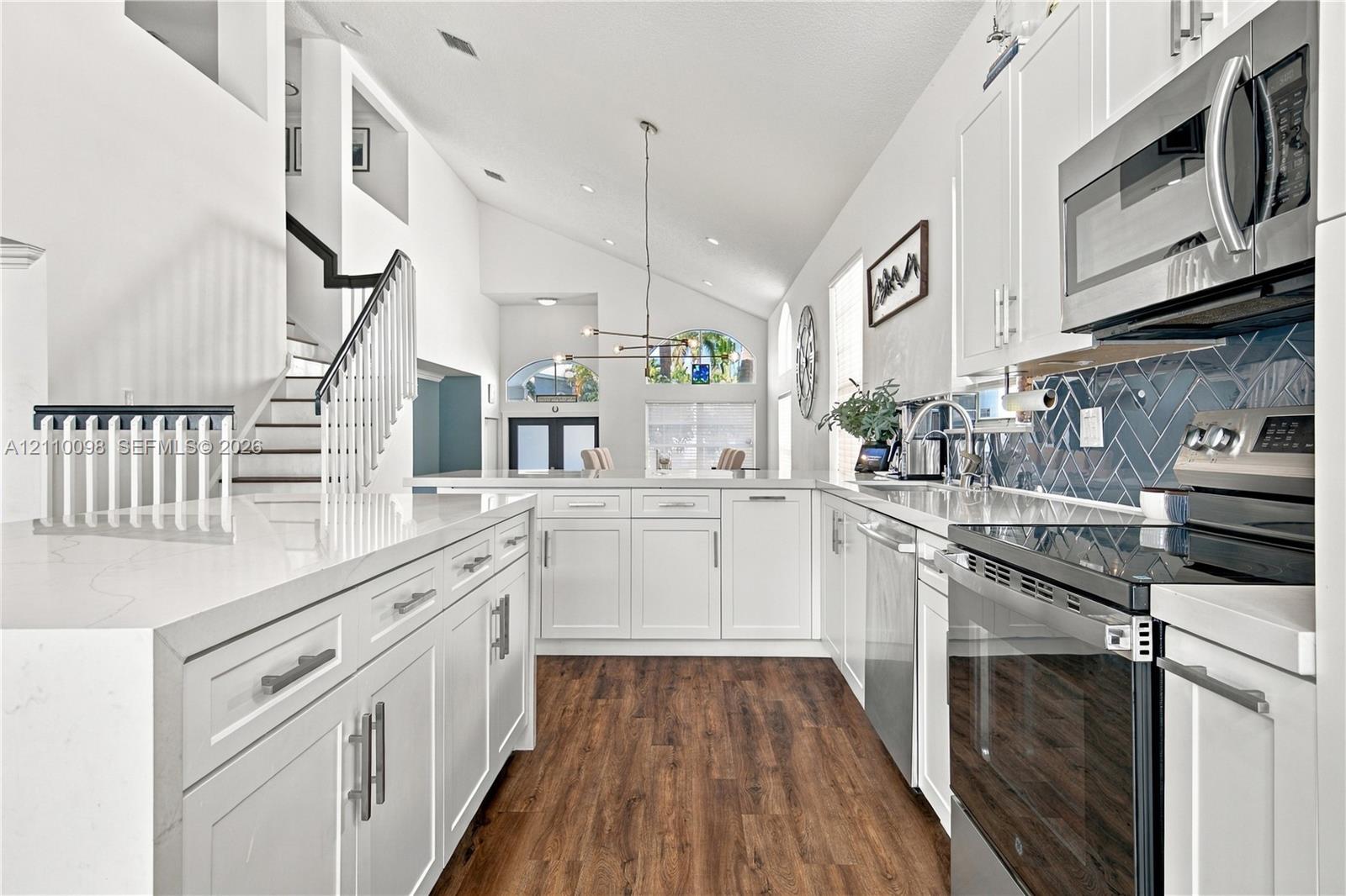 Kitchen featuring white shaker-style cabinetry, quartz countertops, stainless steel appliances, herringbone-patterned tile backsplash, and wood-finish flooring