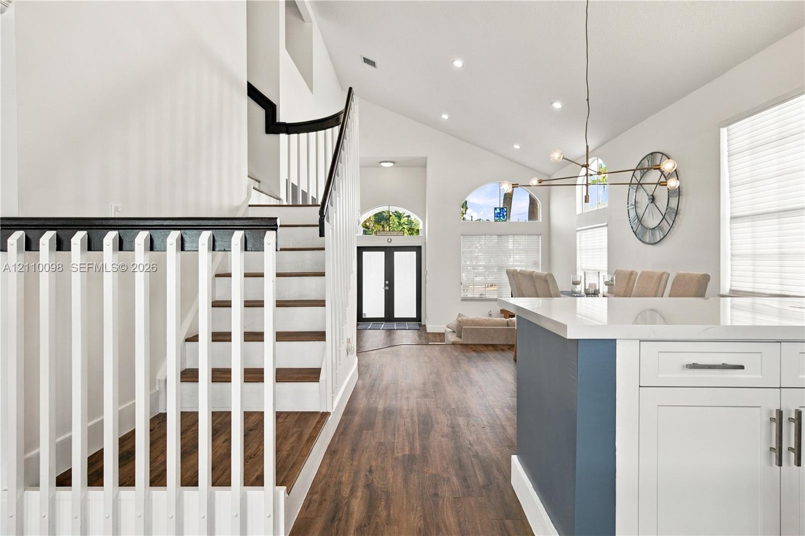 Vaulted ceilings, wood-finish flooring, staircase with contrasting handrail and balusters, architectural arched windows, and kitchen island with white cabinetry