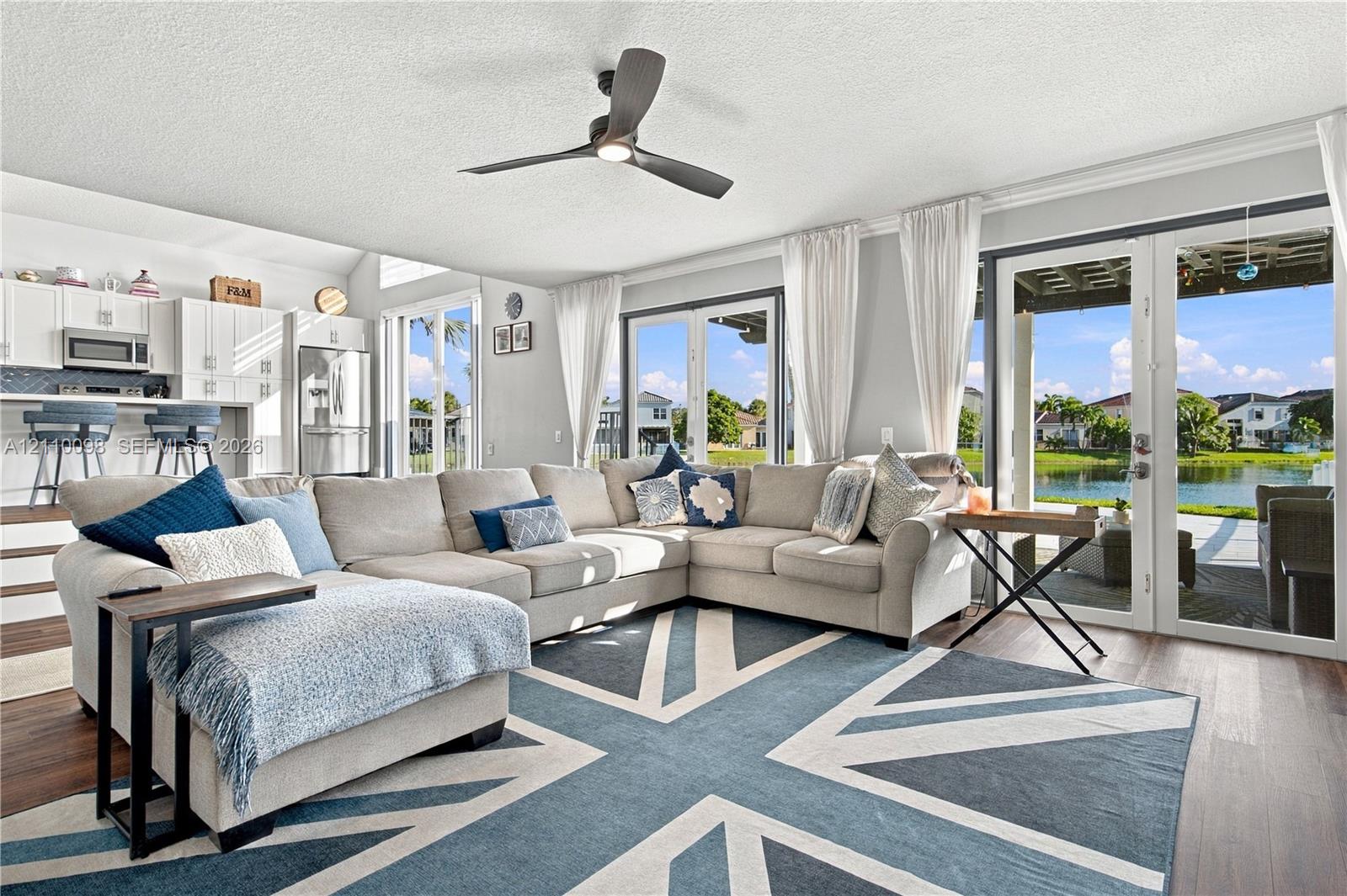 Living space featuring wood-finish flooring, a modern ceiling fan, white cabinetry with built-in stainless steel appliances, and dual glass paneled doors providing exterior access