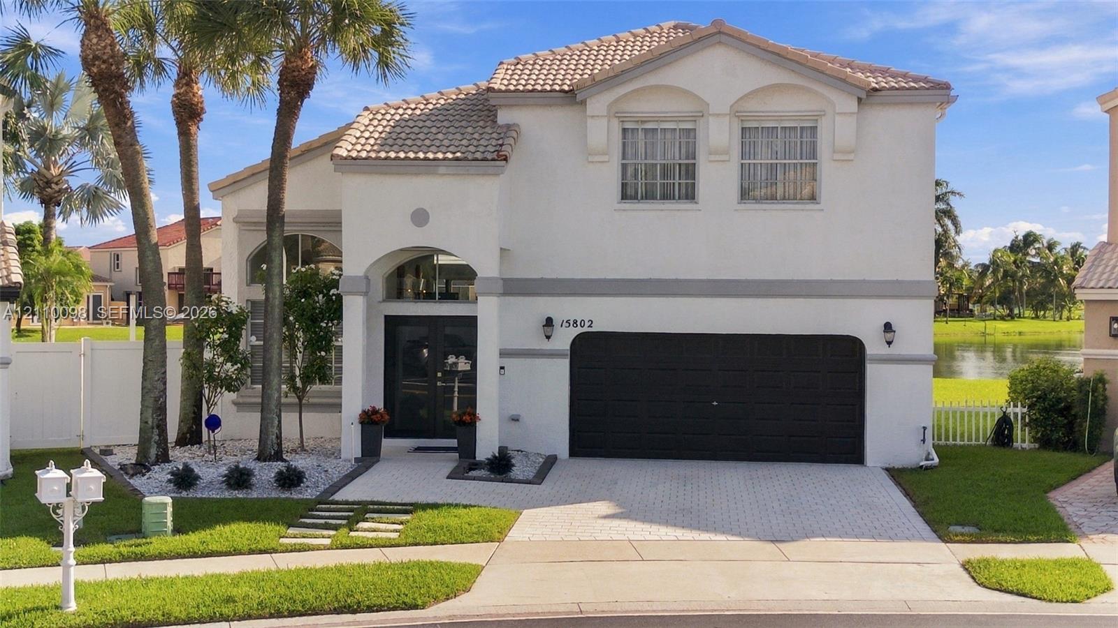 Two-story residence featuring a tile roof, arched entryway, paved driveway, multi-car garage, and waterfront surroundings