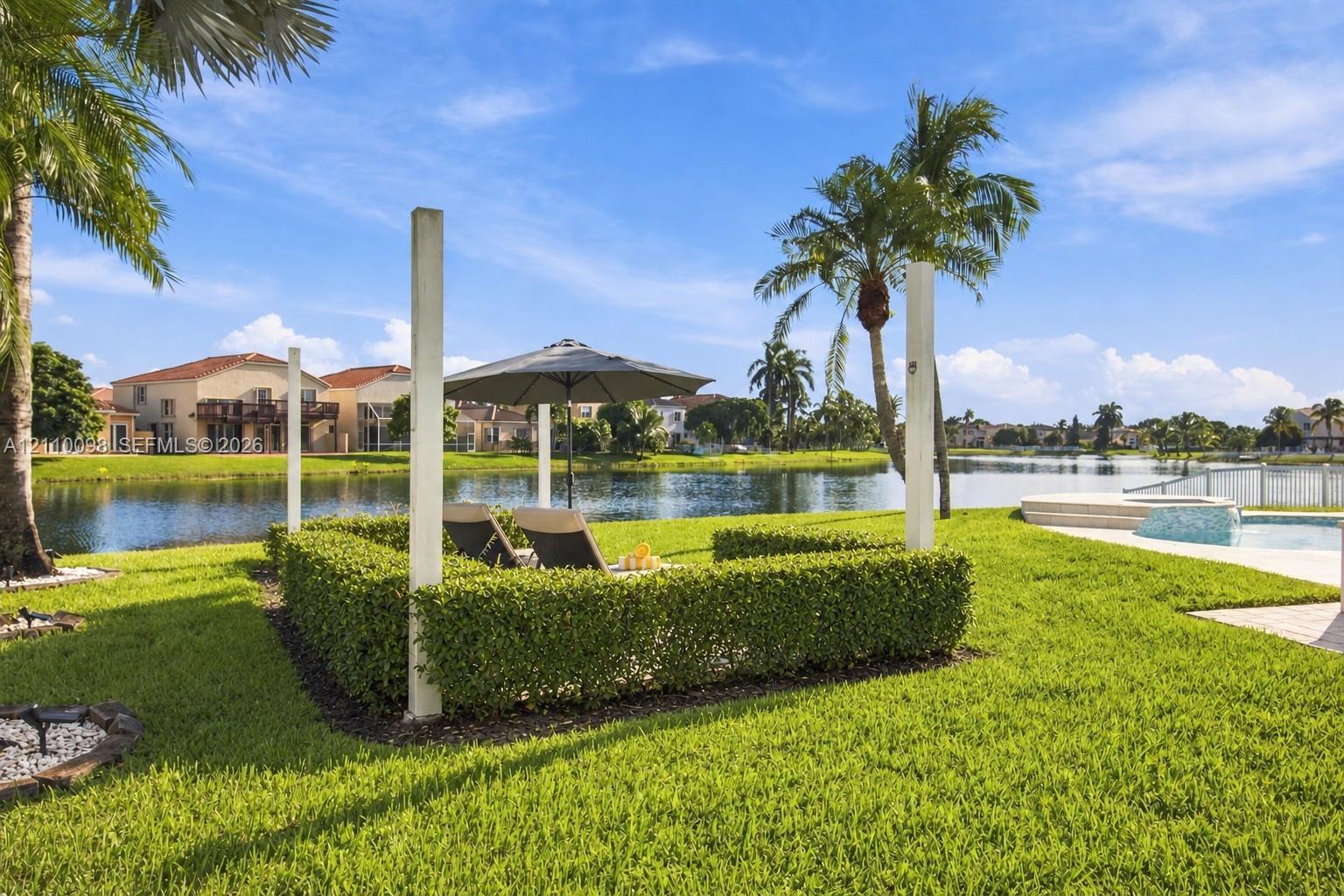 Waterfront backyard featuring a manicured lawn, established landscaping, perimeter fencing, and an inground pool with a tiled spa