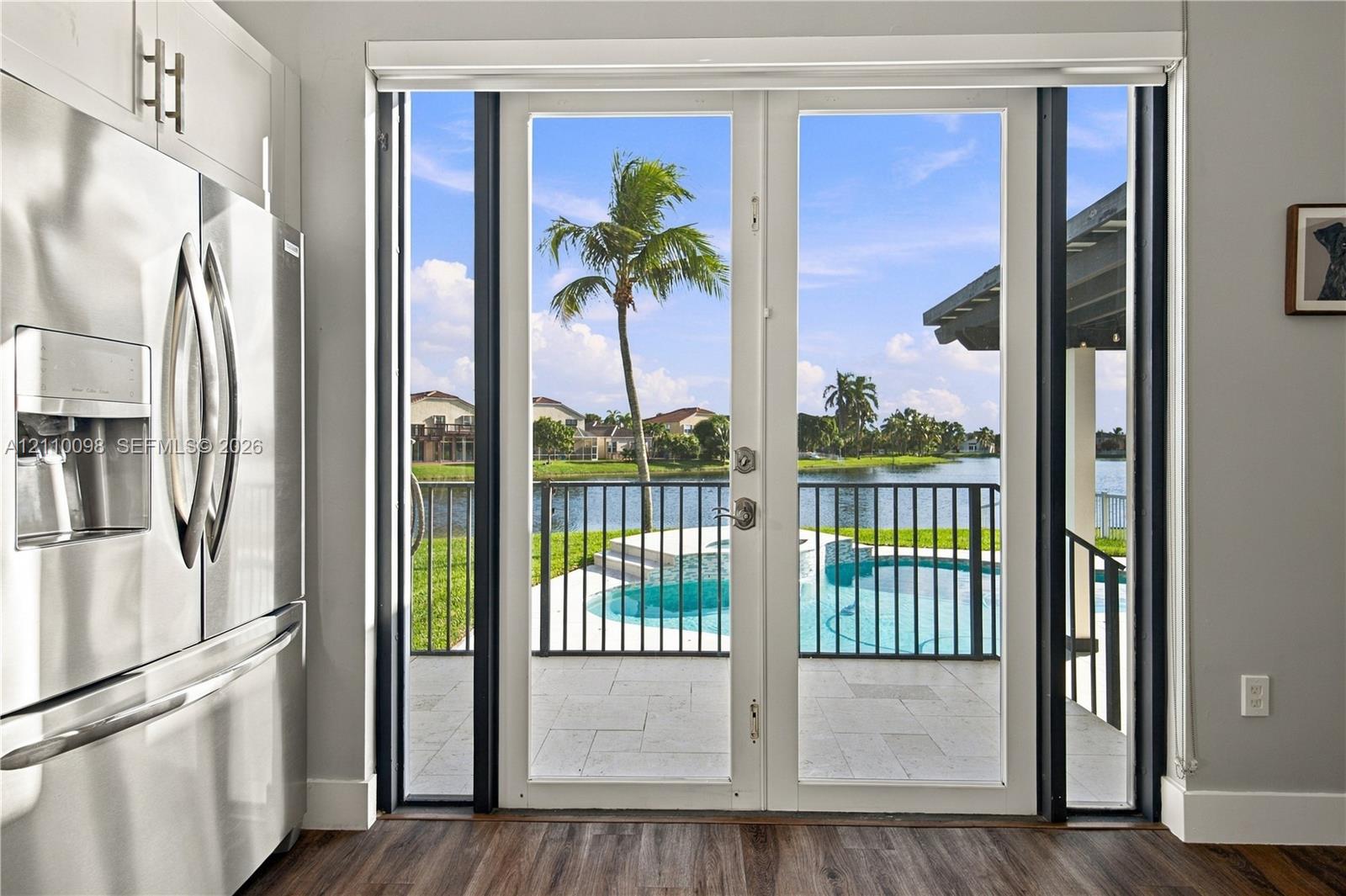 Stainless steel refrigerator, glass-paned double doors, patio with stone-finish pavers, private swimming pool, and water-facing iron fencing