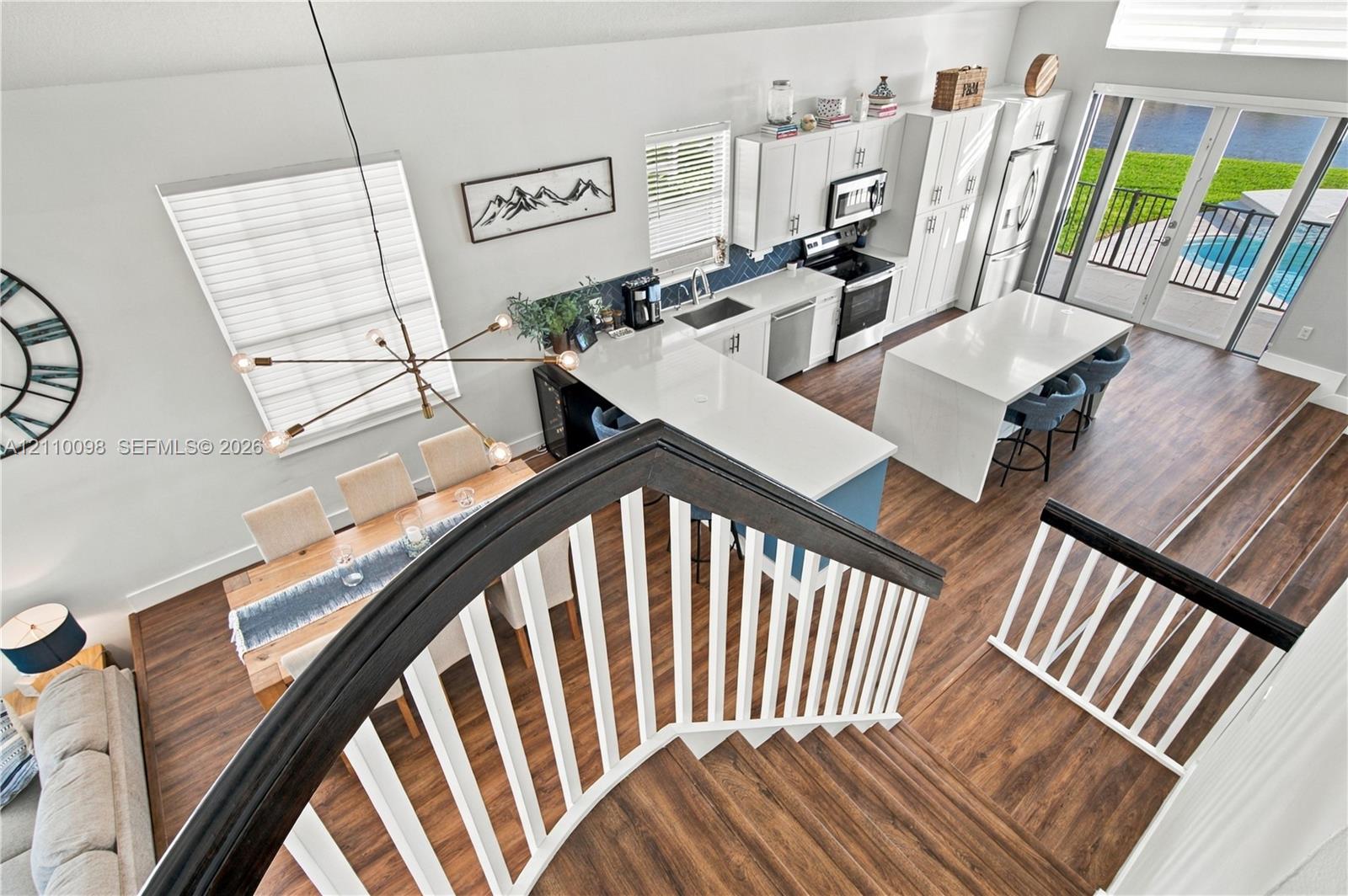 Open-concept kitchen featuring quartz countertops, white shaker-style cabinetry, stainless steel appliances, and a matching kitchen island