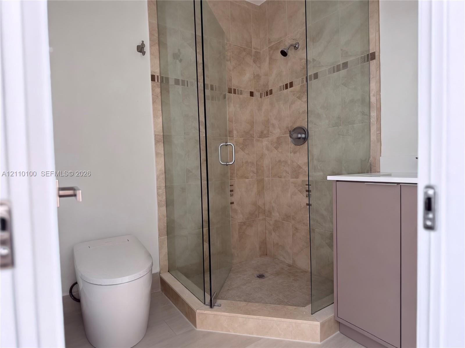 Corner shower enclosure with glass doors, neutral tile surround, accent tile inlay, and integrated vanity featuring a light-toned countertop Corner shower enclosure with glass doors, neutral tile surround, accent tile inlay, and integrated vanity featuring a light-toned countertop