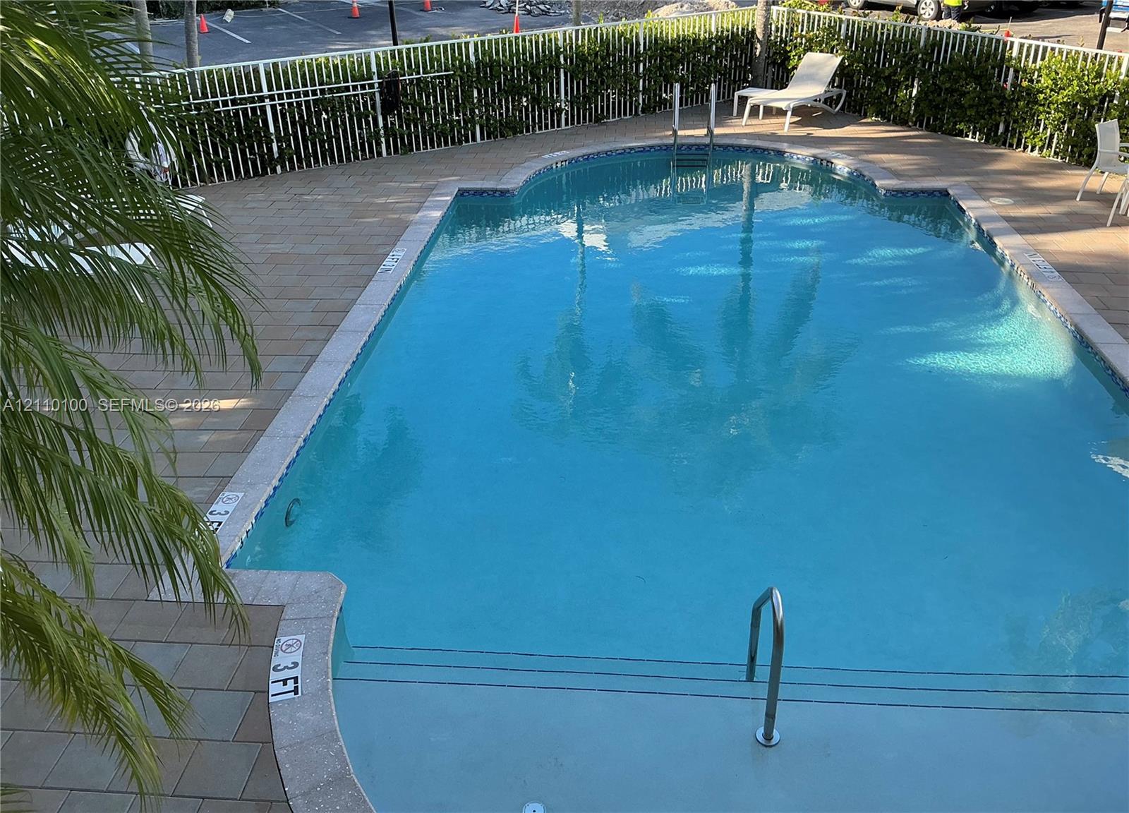 In-ground swimming pool featuring a tiled deck, decorative pool coping, metal handrails, and a perimeter fence