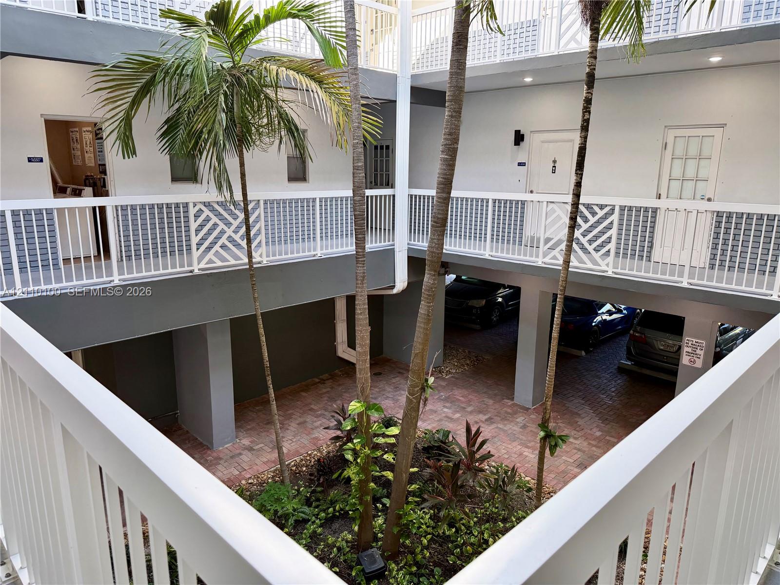 Central courtyard featuring brick pavers, mature palm trees, multi-level exterior walkways with white railings, and covered ground-level parking