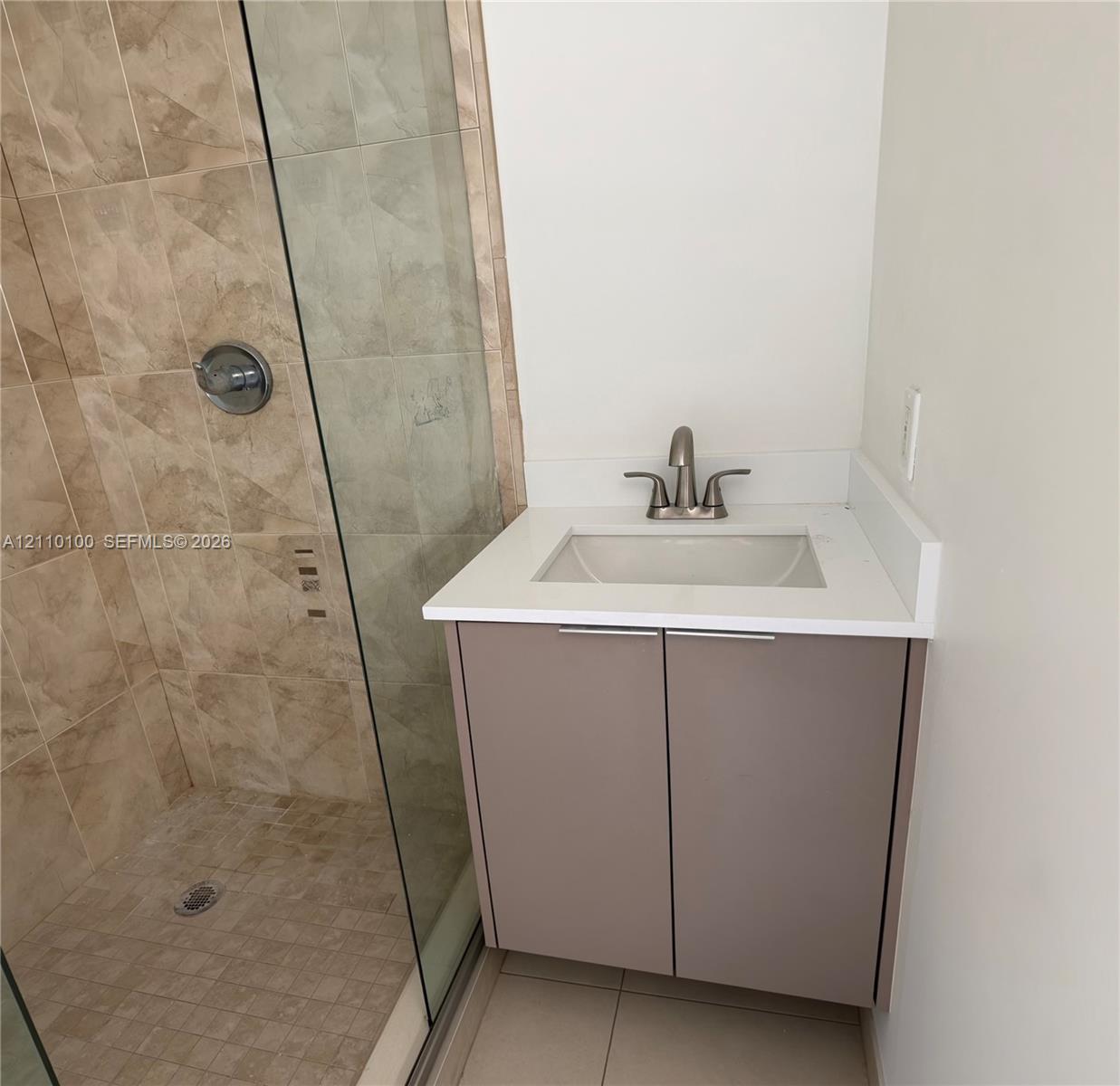 Floating vanity with a light-toned solid surface countertop, undermount sink, brushed nickel faucet, and a walk-in shower featuring glass enclosure and full-height stone-finish wall tile Floating vanity with a light-toned solid surface countertop, undermount sink, brushed nickel faucet, and a walk-in shower featuring glass enclosure and full-height stone-finish wall tile