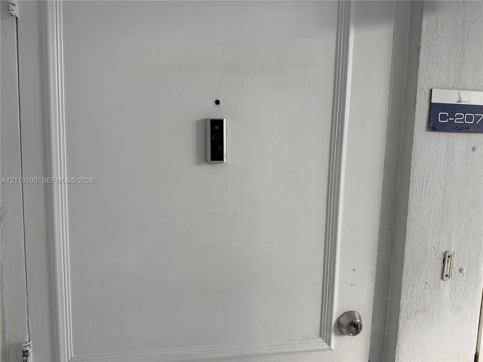 White paneled entry door equipped with a mounted smart doorbell and circular deadbolt lock