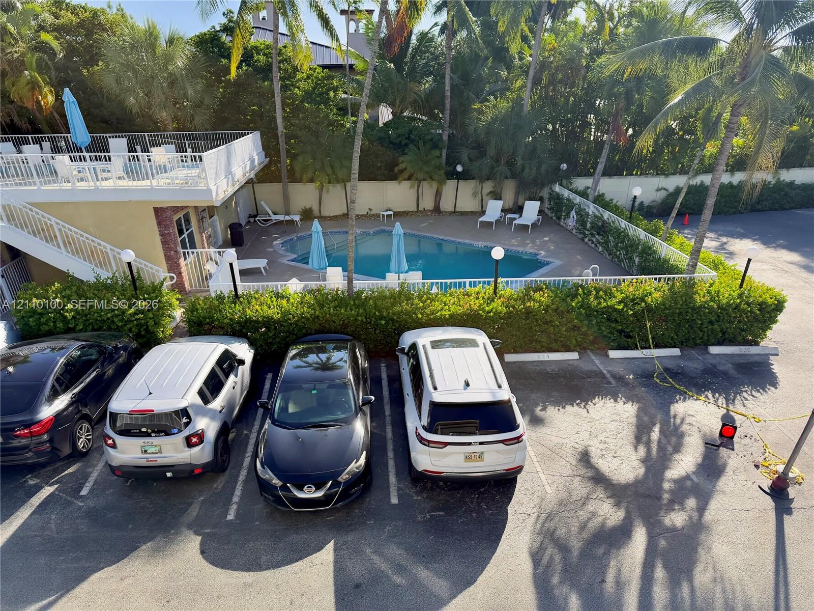 Outdoor pool with concrete decking, second-level balcony, and exterior perimeter fencing surrounded by mature palm trees