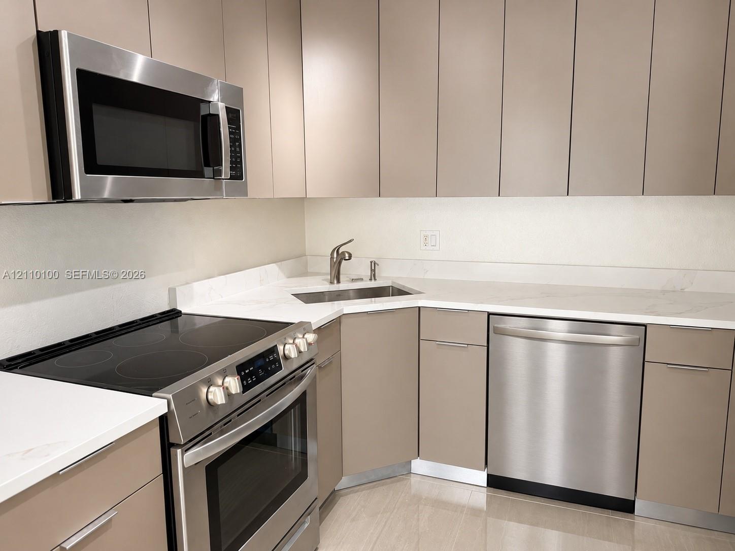 Kitchen featuring matte-finish flat-panel cabinetry, light-toned stone-style countertops, stainless steel appliances, a built-in microwave, and an undermount corner sink with a high-arch faucet