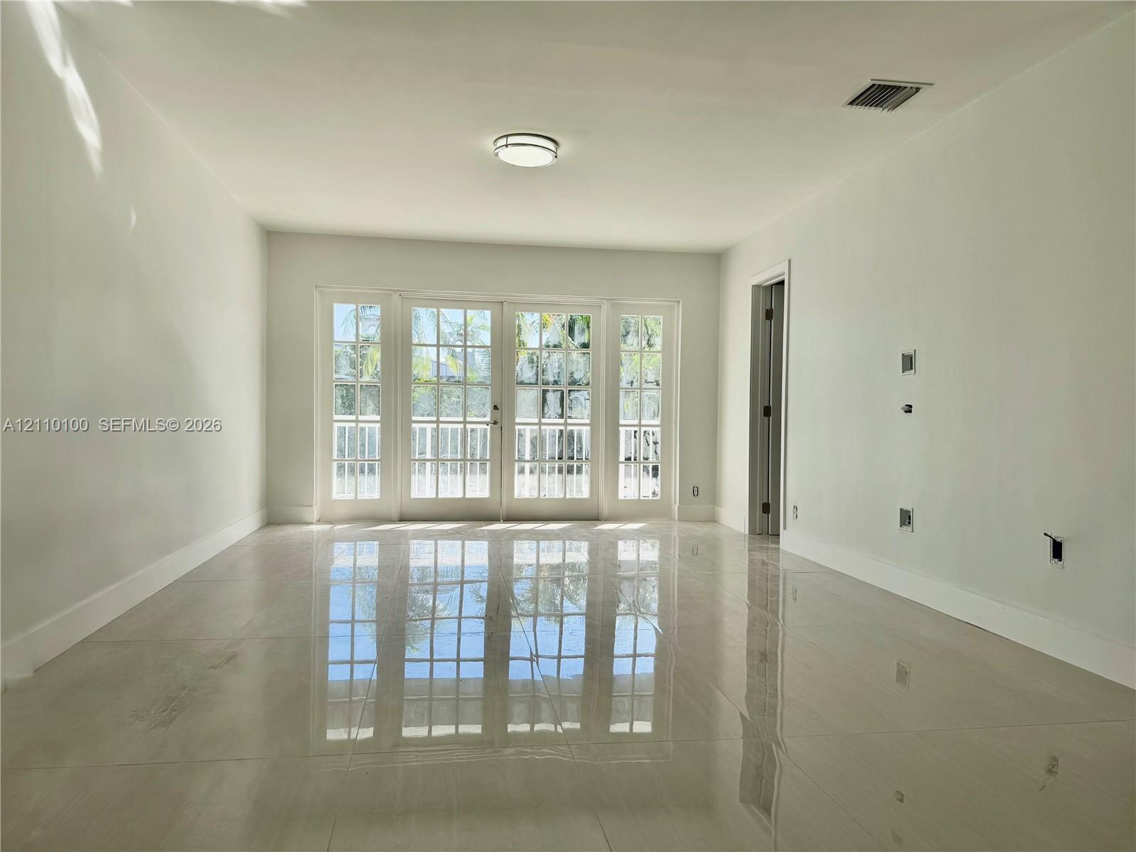 Interior space featuring polished tile flooring, white wall finishes, flush-mount ceiling lighting, and a multi-pane glass-panel door system Interior space featuring polished tile flooring, white wall finishes, flush-mount ceiling lighting, and a multi-pane glass-panel door system