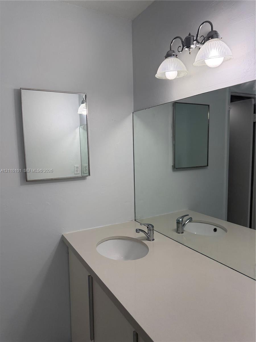 Vanity featuring a solid-surface countertop, integrated basin, polished metal faucet, large wall-mounted mirror, and decorative dual-light fixture