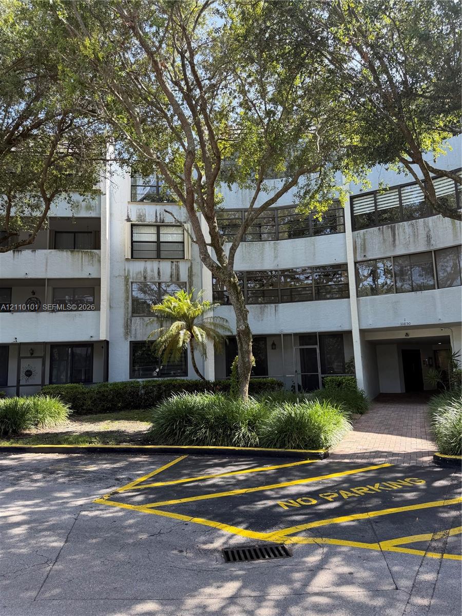 Multi-story facade with expansive horizontal window banks, integrated balconies, and brick-paved walkway