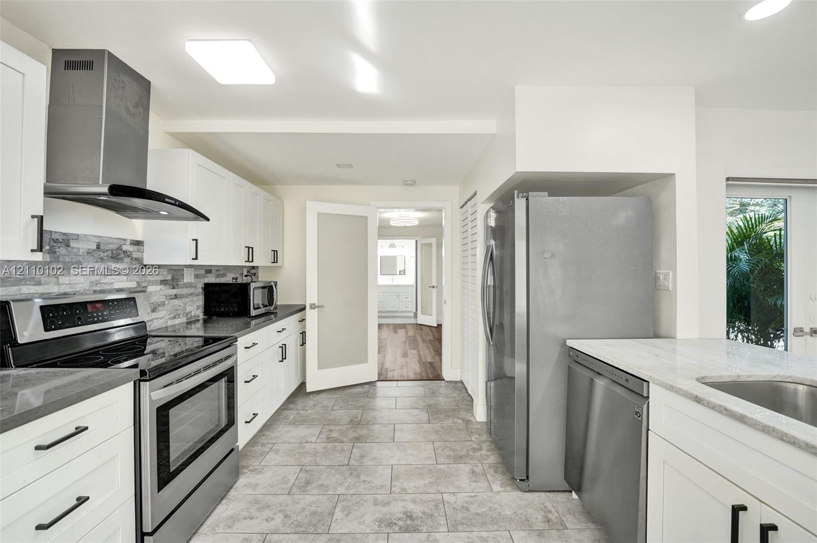 Kitchen featuring white shaker cabinetry, stone-tile backsplash, stainless steel appliances, stone-look countertops, and neutral tile flooring