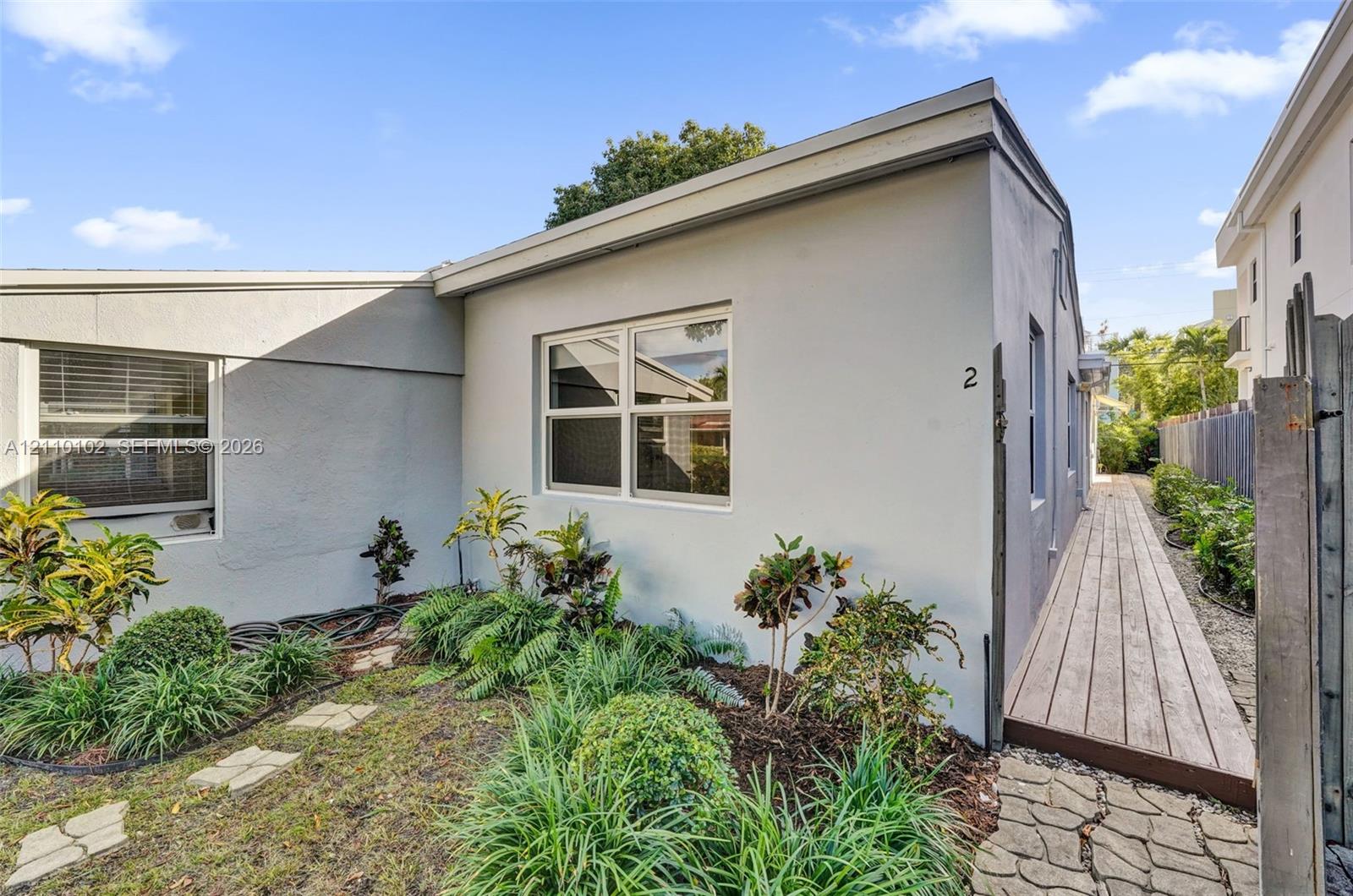 Smooth stucco exterior featuring dual-pane windows, a wooden boardwalk, and a stone-paver walkway bordered by ornamental landscaping