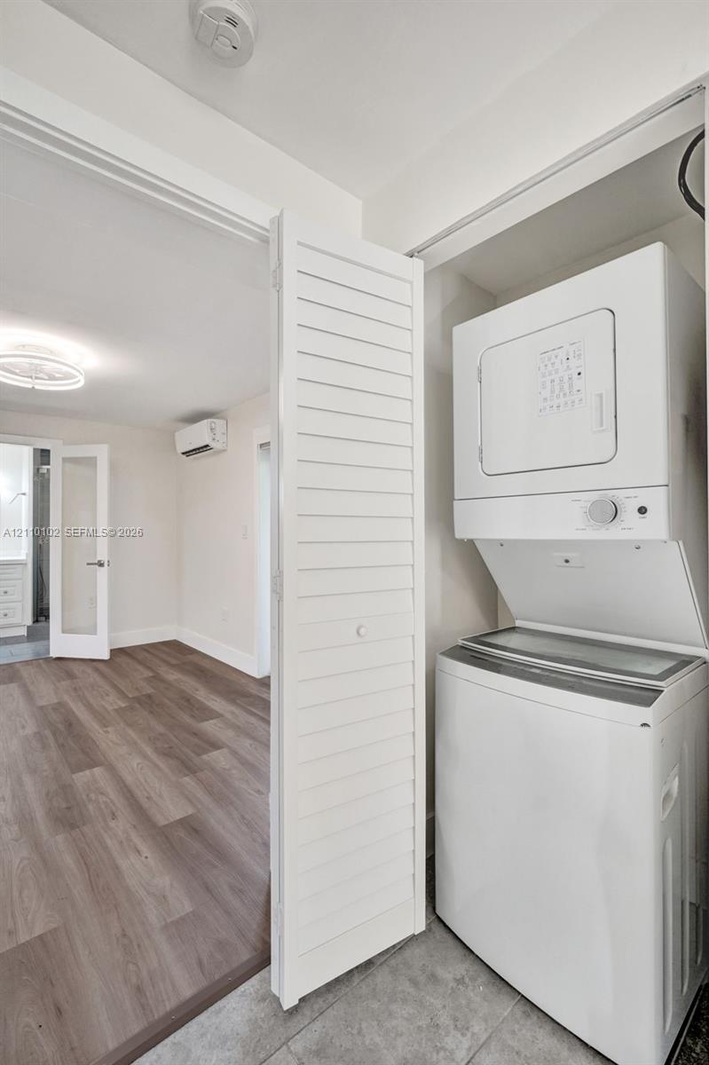 Stackable laundry unit featuring a top-load washer and front-load dryer set behind white louvered closet doors, complemented by wood-finish flooring and a wall-mounted ductless climate control system