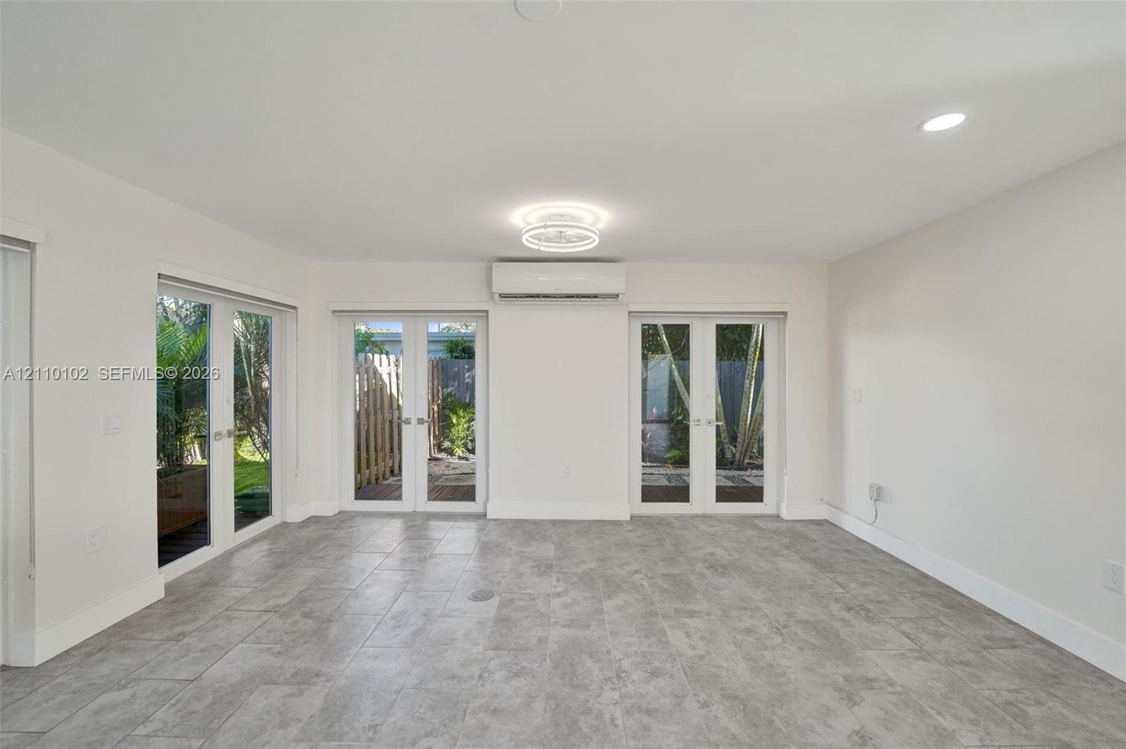 Neutral-toned tile flooring, dual sets of glass-paned French doors, wall-mounted ductless climate control unit, and recessed ceiling lighting