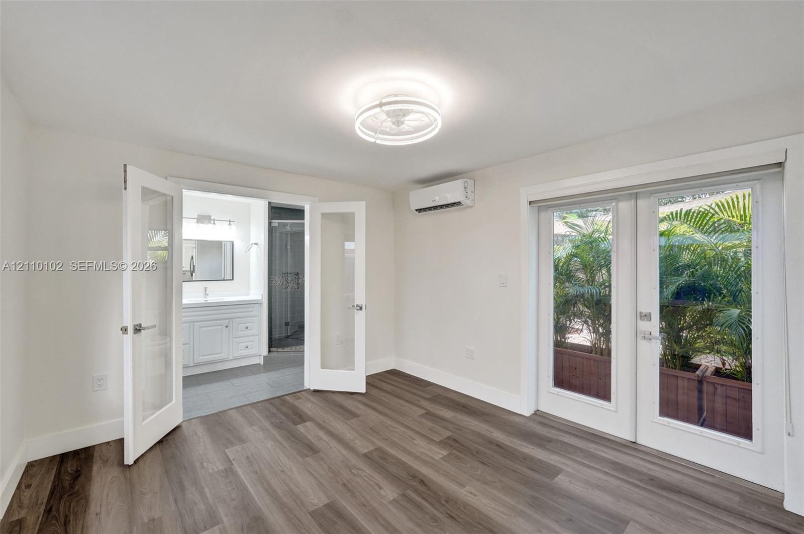 Wood-finish flooring, white double French doors, wall-mounted climate control unit, circular flush-mount ceiling light fixture, and glass-paneled exterior door