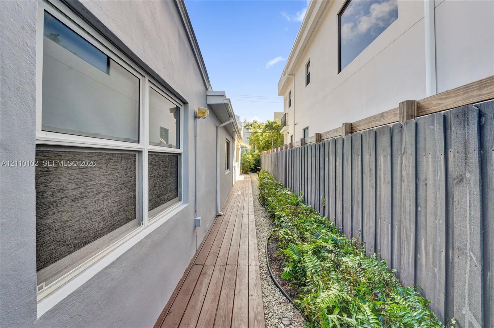 Exterior side walkway featuring wood-plank decking, a vertical wood privacy fence, and integrated landscaping with stone ground cover