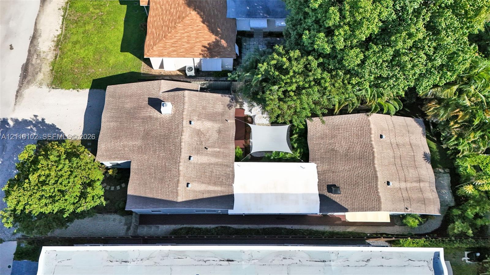 Aerial perspective of a multi-section roofline featuring asphalt shingles, a central paved courtyard, and mature perimeter trees