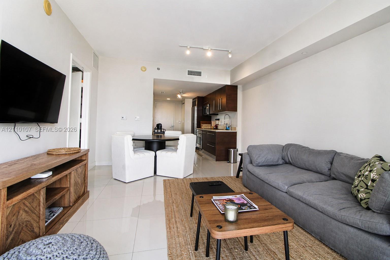 Open concept area featuring large-format tile flooring, recessed track lighting, and a kitchen equipped with dark wood-finish cabinetry and stainless steel appliances