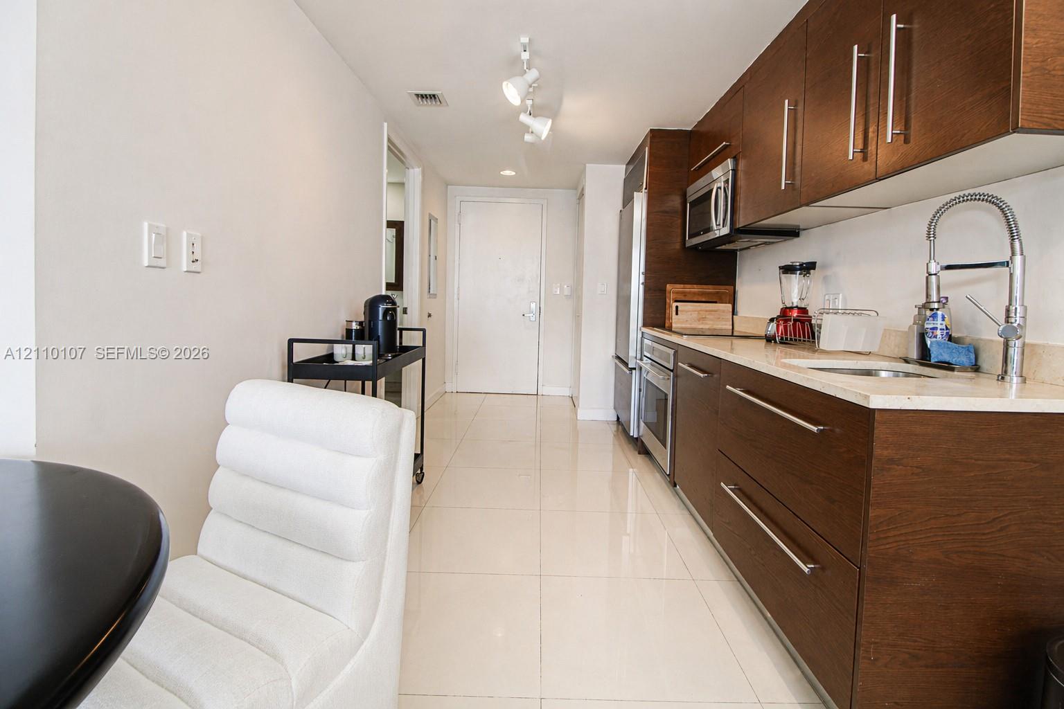Kitchen featuring flat-panel wood-finish cabinetry, light-toned stone countertops, stainless steel appliances, polished tile flooring, and a gooseneck faucet