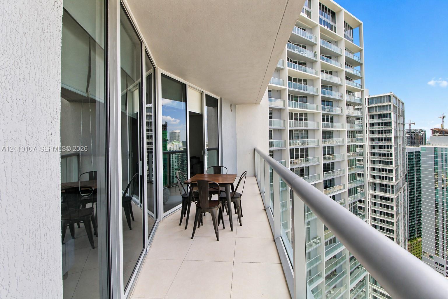 Covered balcony featuring expansive glass sliding door entry, floor-to-ceiling windows, and a glass-paneled railing