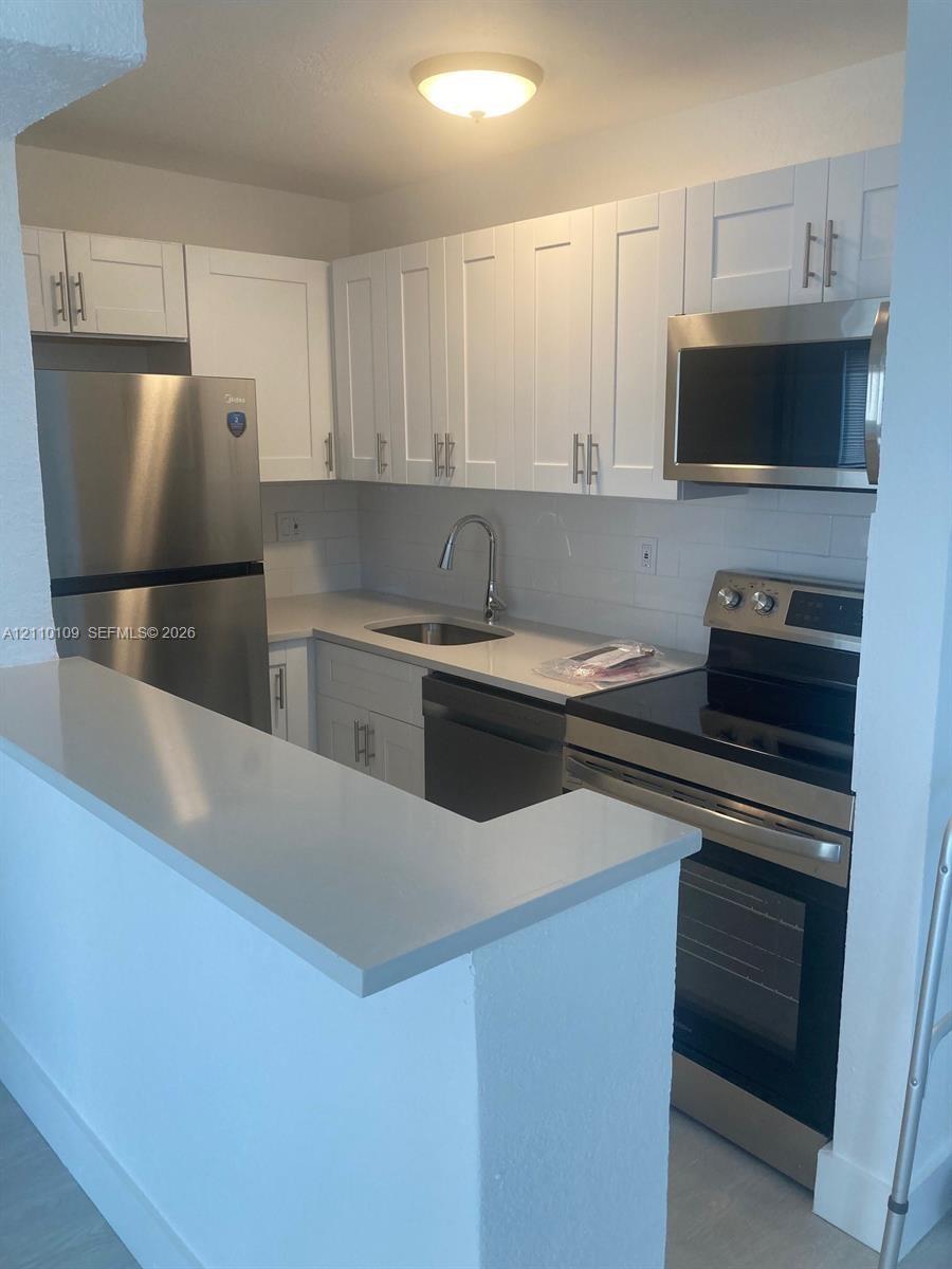 Kitchen featuring white shaker-style cabinetry, quartz countertops, stainless steel appliances, and a peninsula with breakfast bar seating