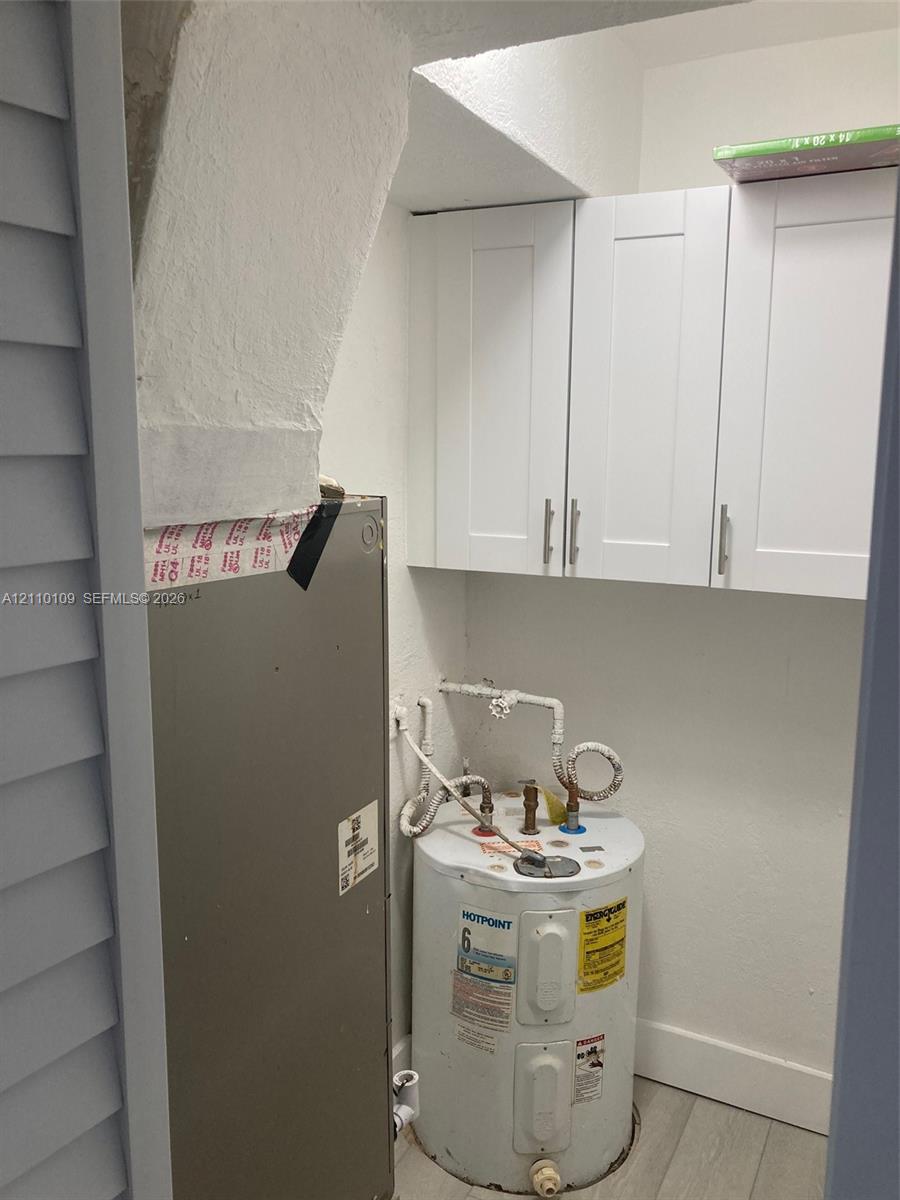 Utility area featuring white shaker-style wall cabinets, a water heater, and an integrated HVAC unit