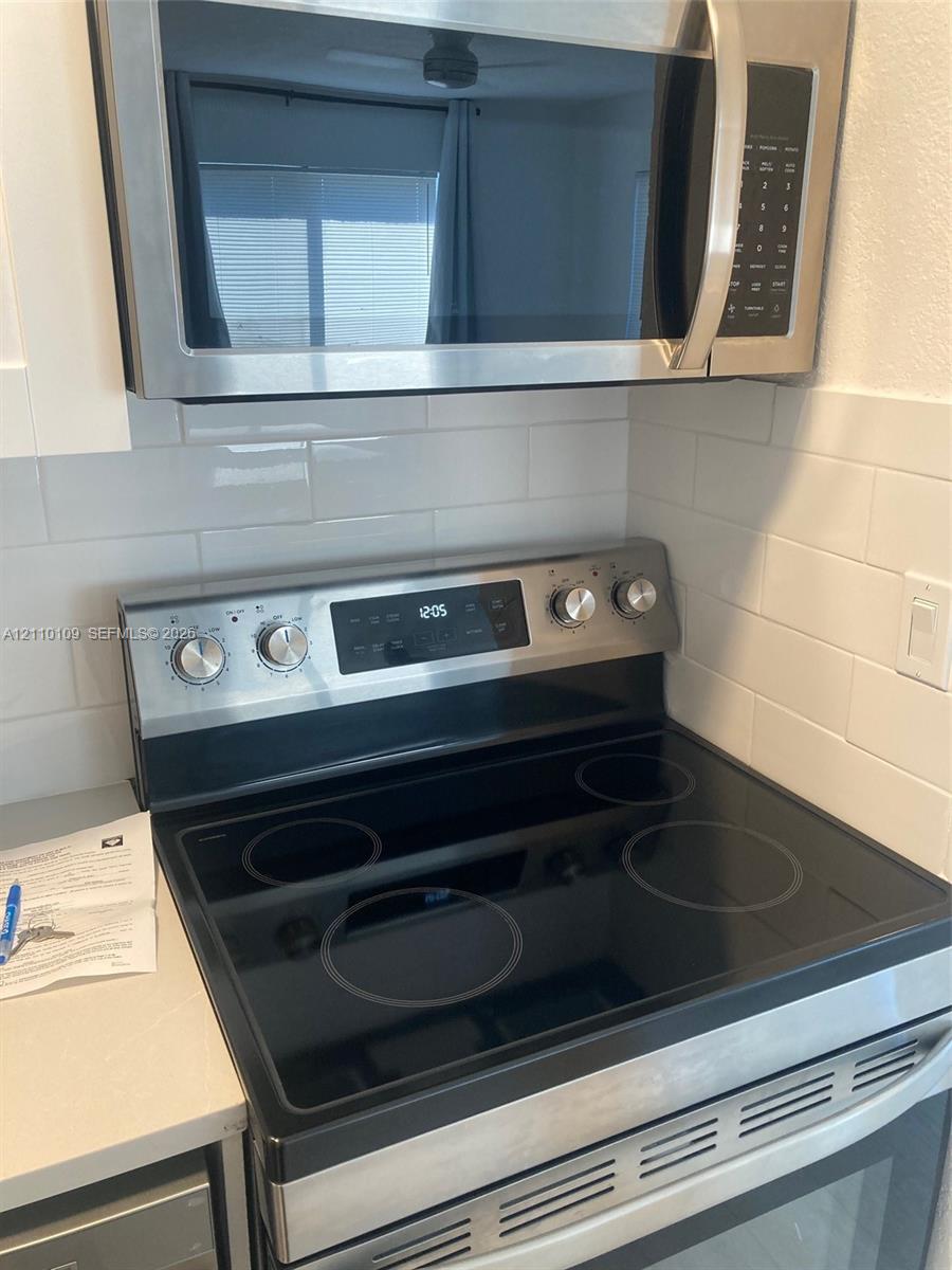 Stainless steel electric range and built-in microwave, white subway tile backsplash, and solid surface countertop