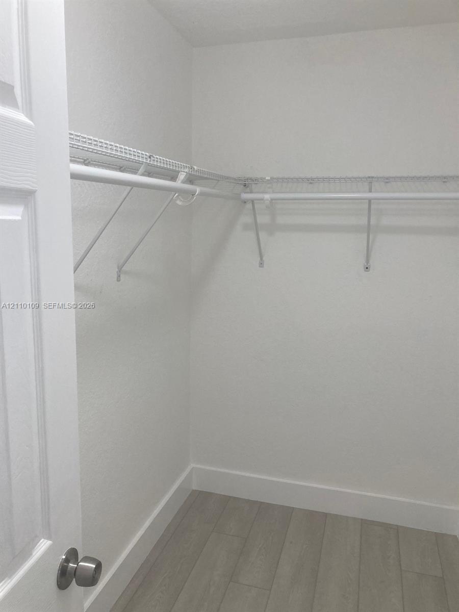 Storage area featuring neutral wood-finish flooring and white wire shelving with integrated hanging rods