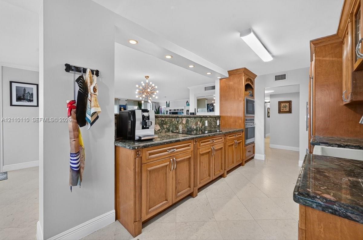 Kitchen featuring medium-tone wood cabinetry, stone countertops, integrated wall ovens, recessed lighting, and tile flooring