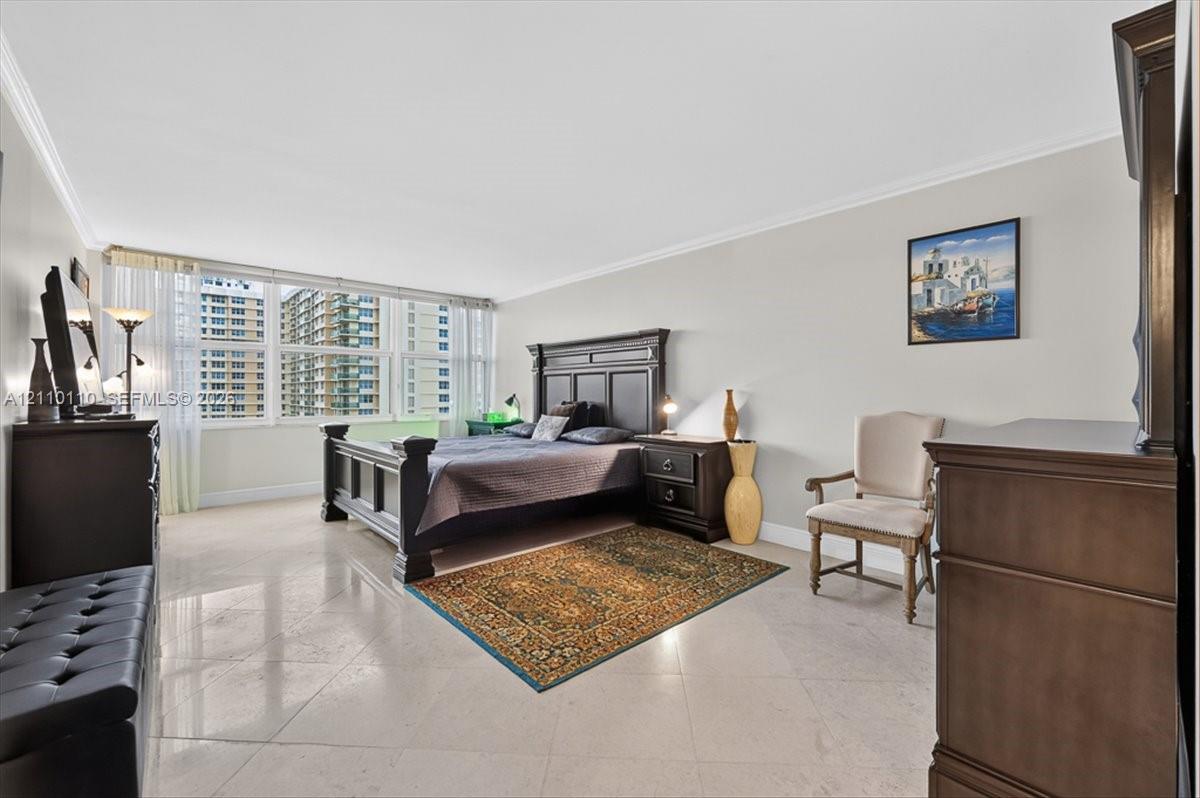 Spacious room featuring polished stone flooring, crown molding, and floor-to-ceiling windows