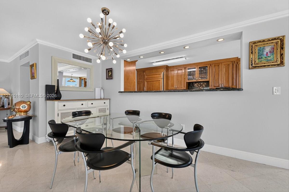Dining area featuring stone flooring, a decorative multi-bulb pendant fixture, crown molding, and a pass-through opening with a stone countertop