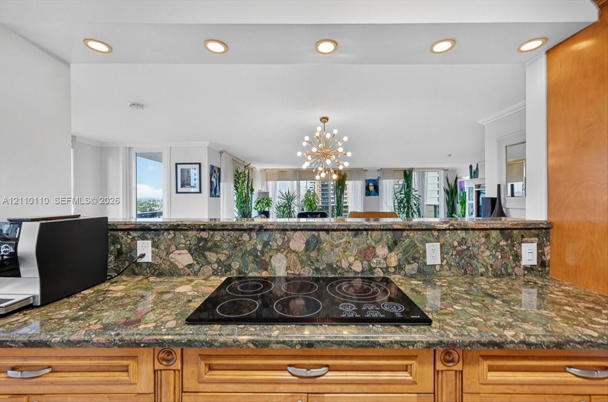 Kitchen featuring multi-tonal stone countertops, backsplash, inset electric cooktop, recessed ceiling lighting, and wood-finish cabinetry