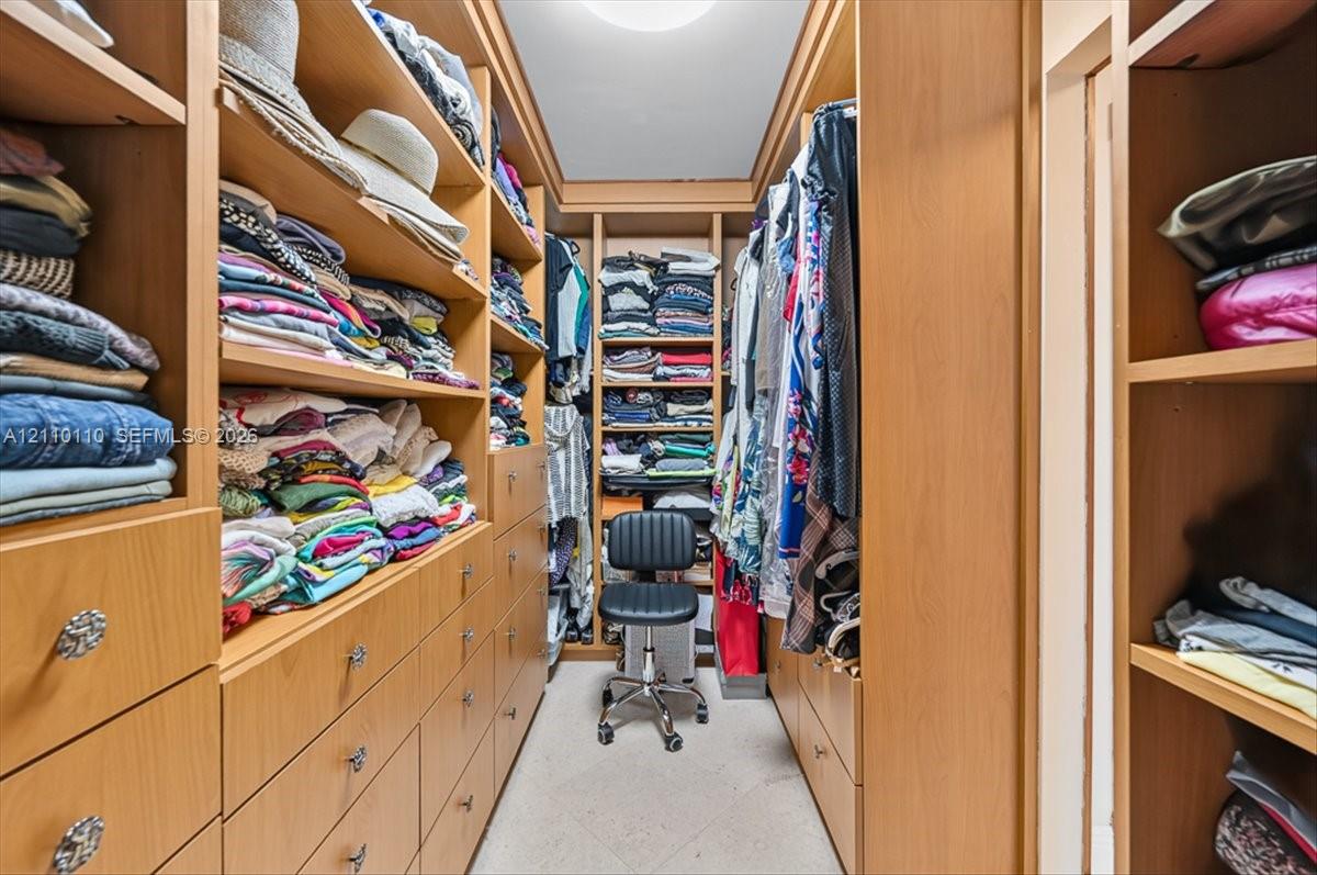 Walk-in closet featuring extensive custom wood-finish built-in cabinetry, floor-to-ceiling shelving, multiple integrated storage drawers, and recessed ceiling lighting