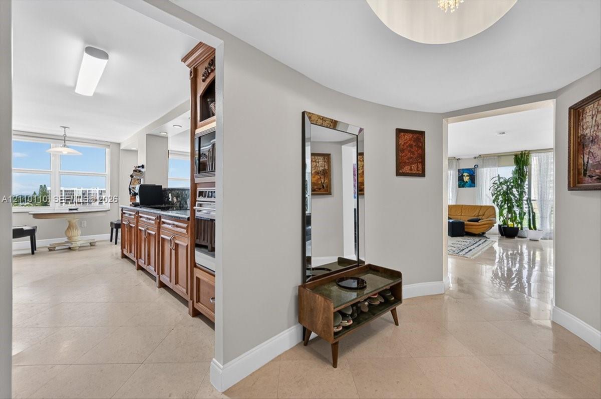 Curved interior wall, polished stone-finish flooring, custom wood cabinetry with integrated built-in oven, and recessed ceiling lighting