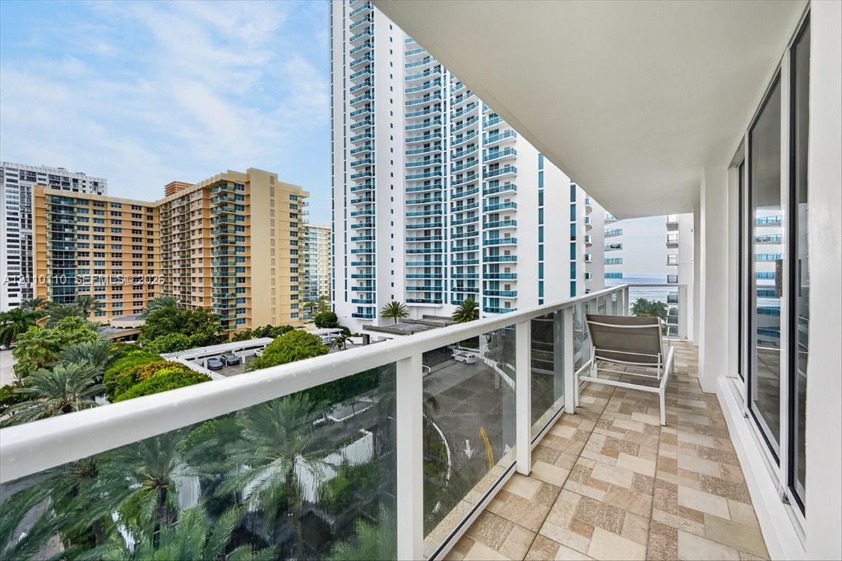 Covered balcony featuring tiled flooring, glass-panel railing, and floor-to-ceiling glass sliding doors