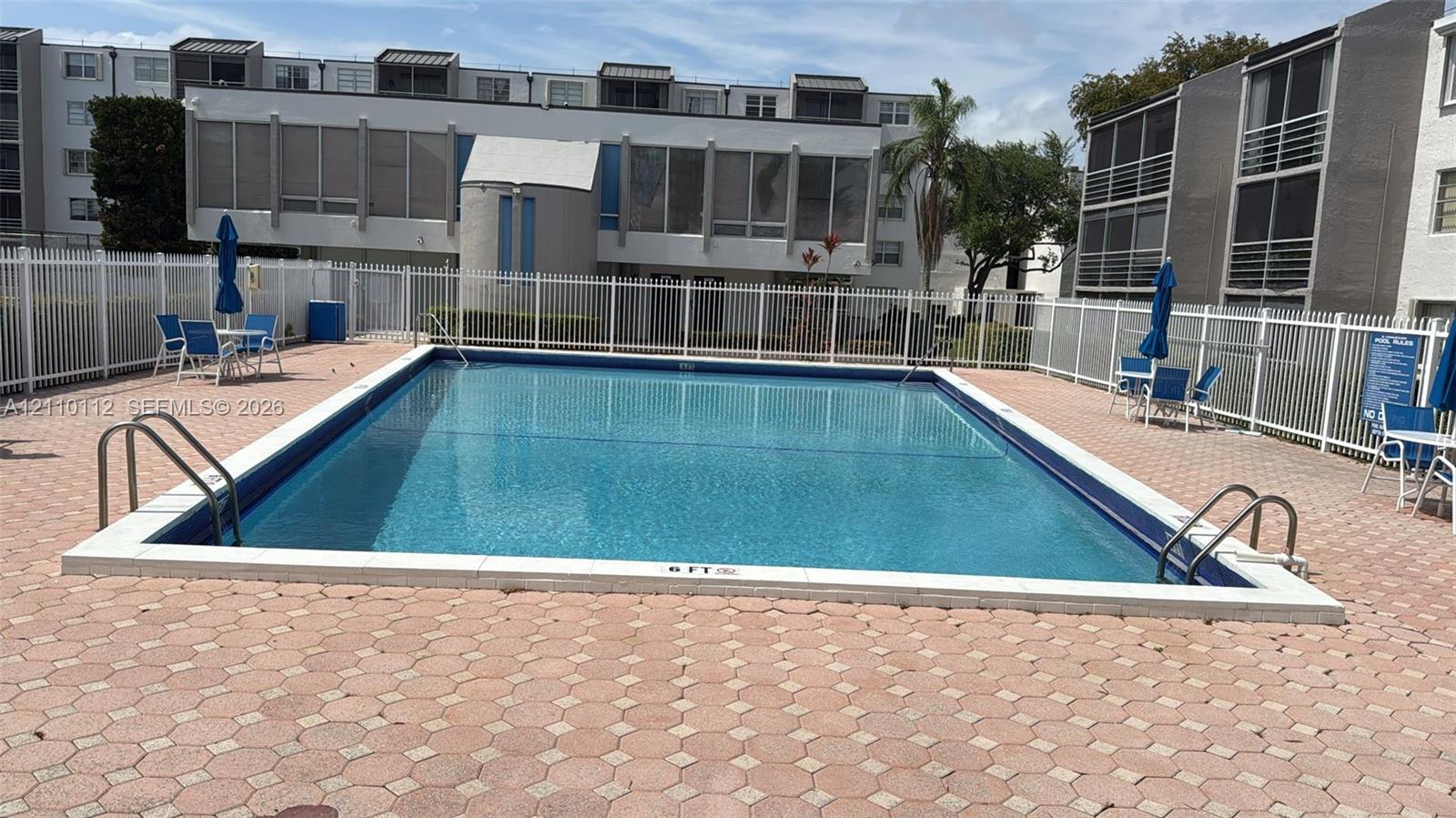 Rectangular swimming pool featuring metal access ladders and a concrete paver deck enclosed by a white fence